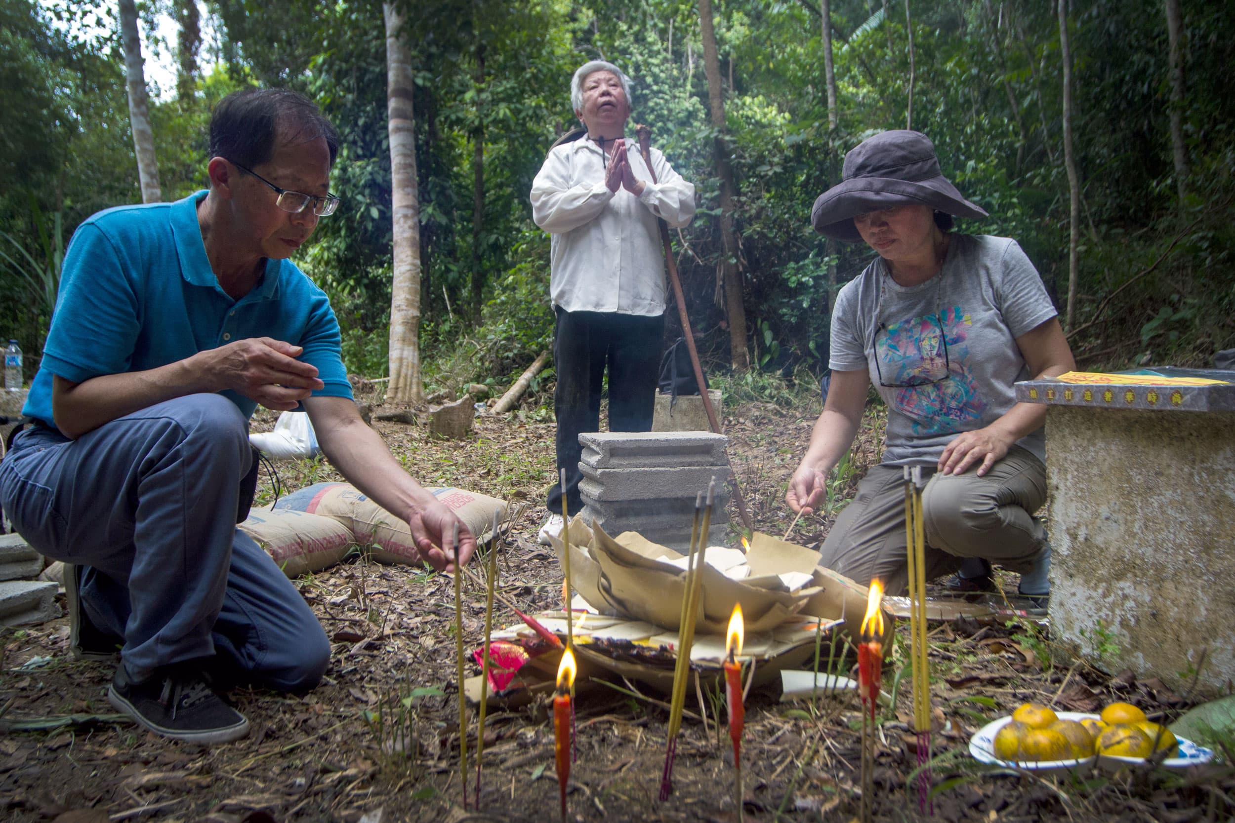 Three people stand in a jungle around a gravestone