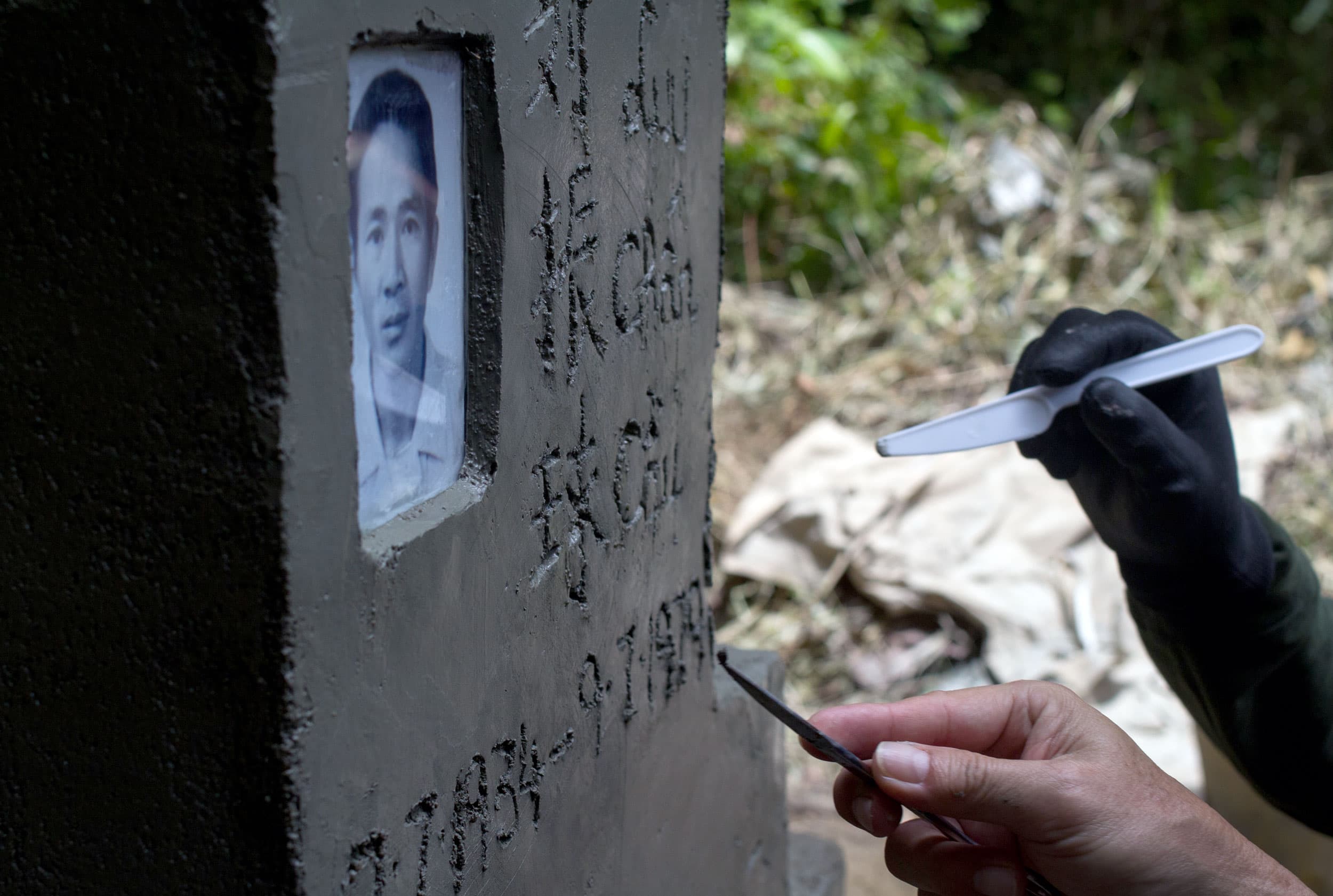 A hand holds a plastic knife and is etching words into a wet tombstone