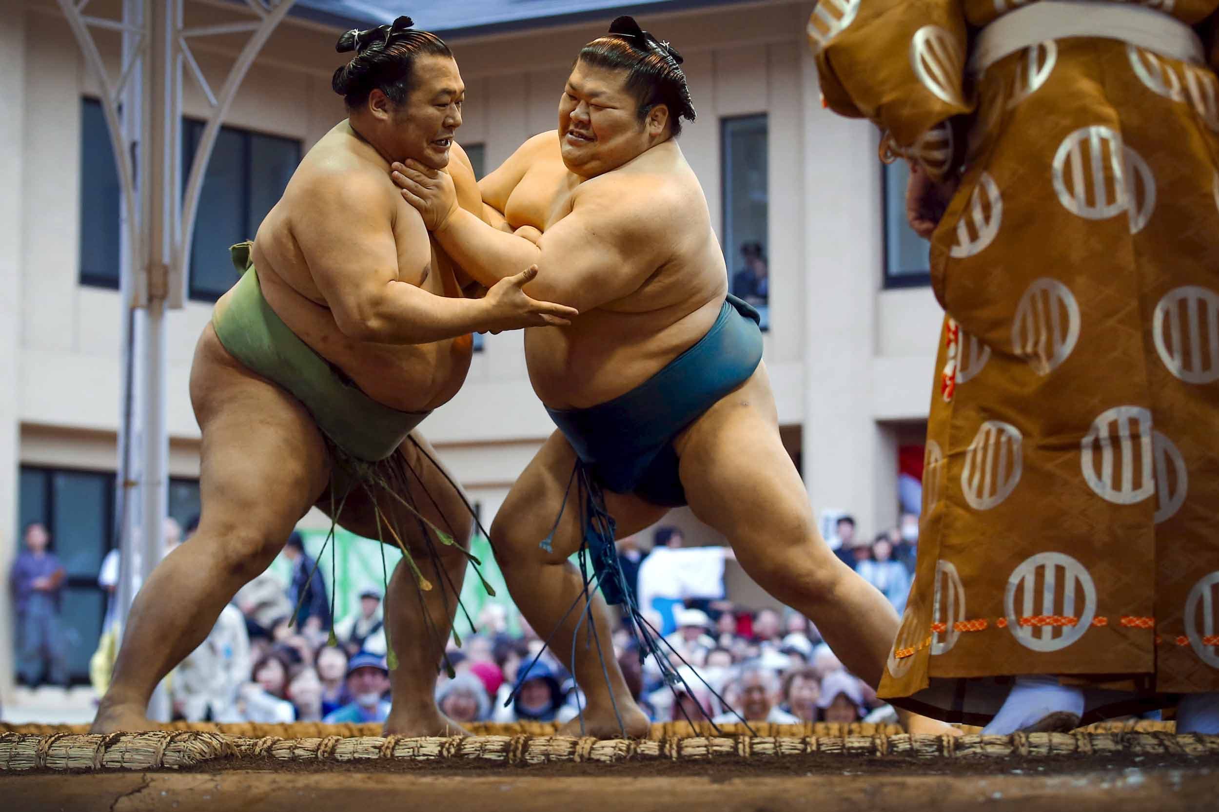 Two sumo wrestlers compete in an outdoor ring while a crowd watches.
