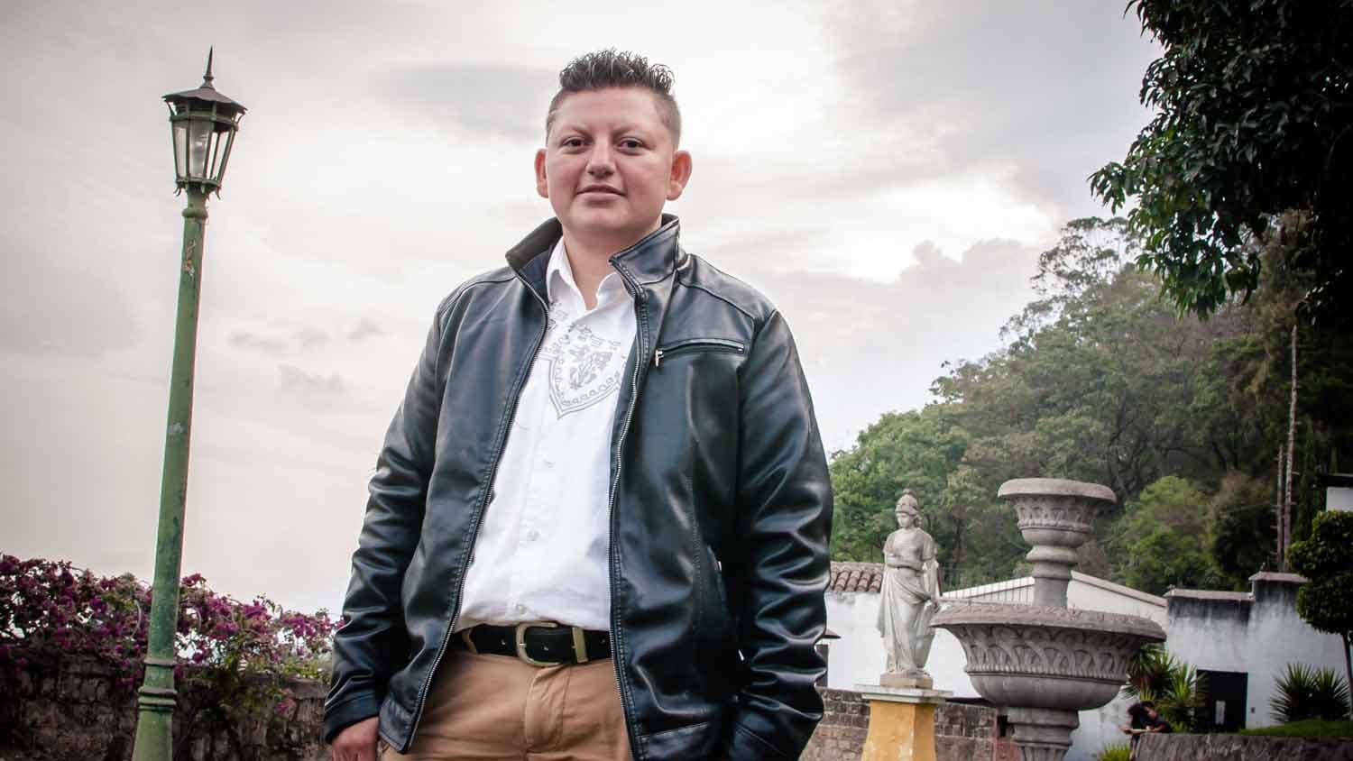 A man wearing a leather coat stands in a public square.