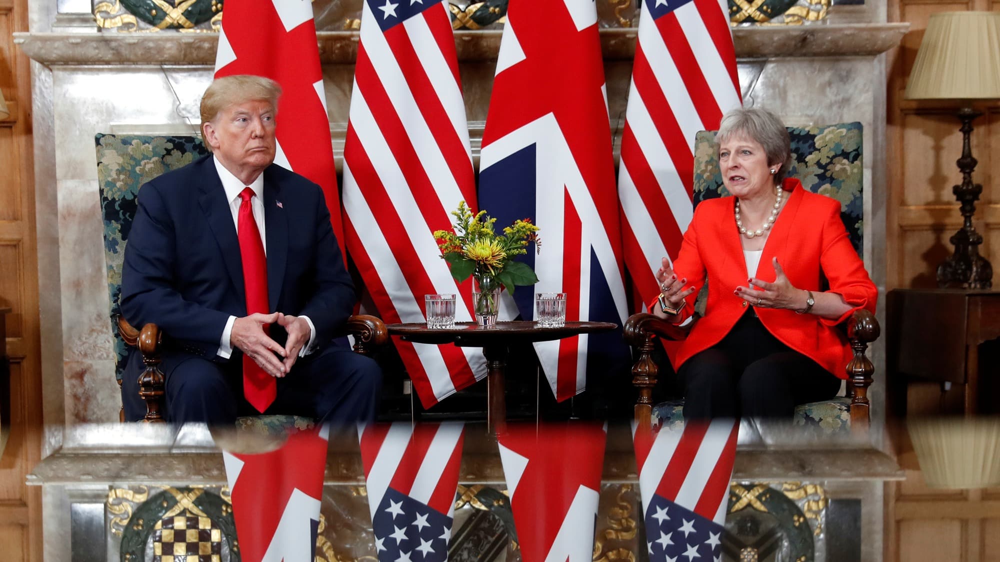 US President Donald Trump is show sitting next to British Prime Minister Theresa May at the end of a table with flags behind them.
