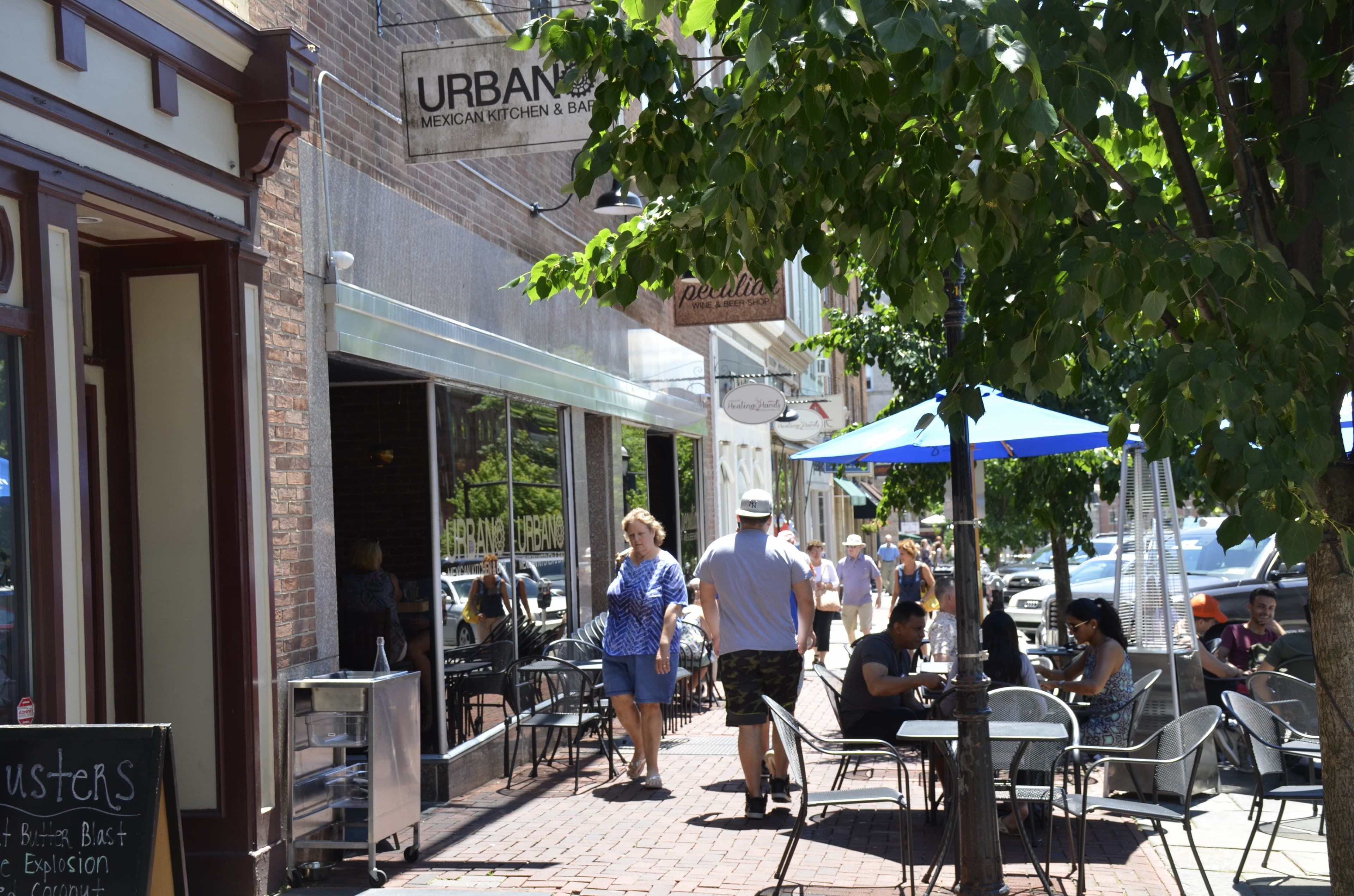 People sit at tables on sidewalks on a city street