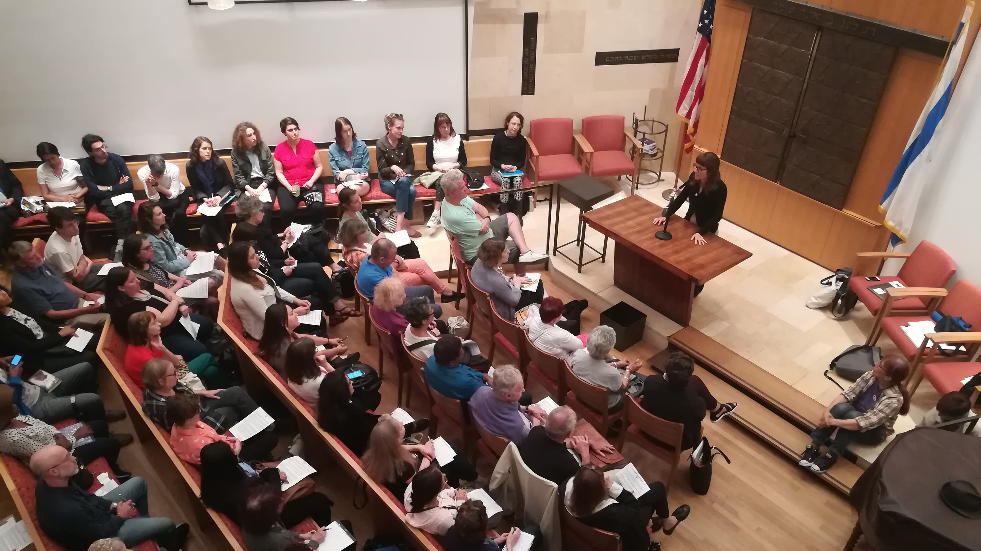 Overhead view of congregation in pews, while woman stands at podium speaking