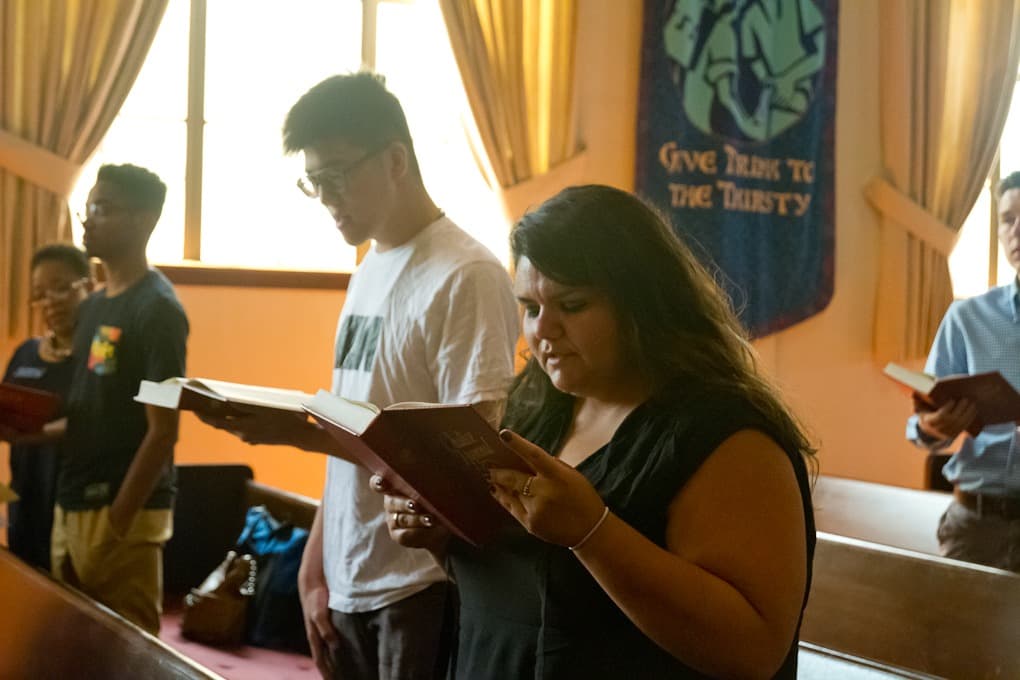 Woman in church holding book and singing, with other congregants behind her