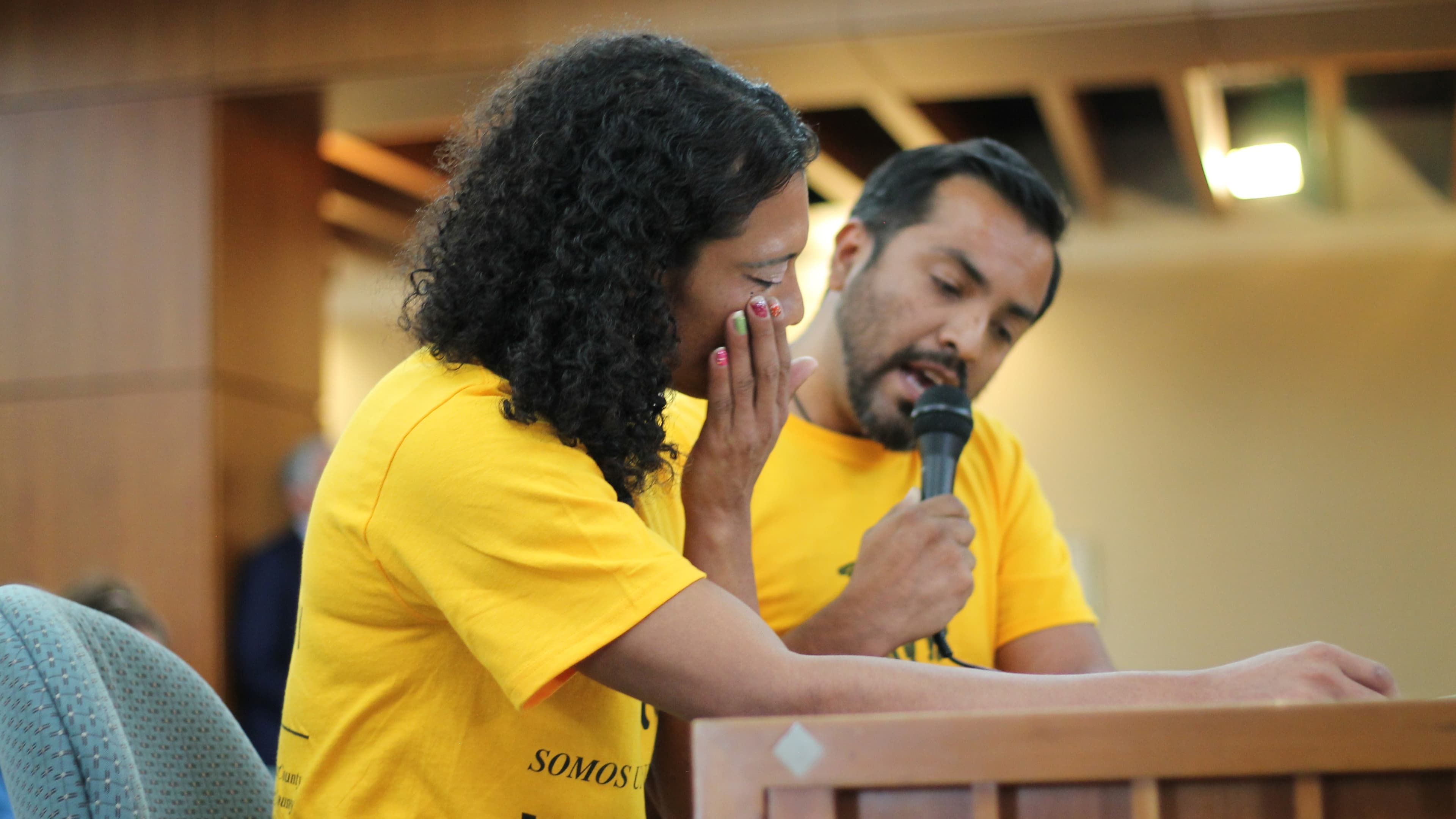 Woman at podium wipes away tears, while man stands next to her