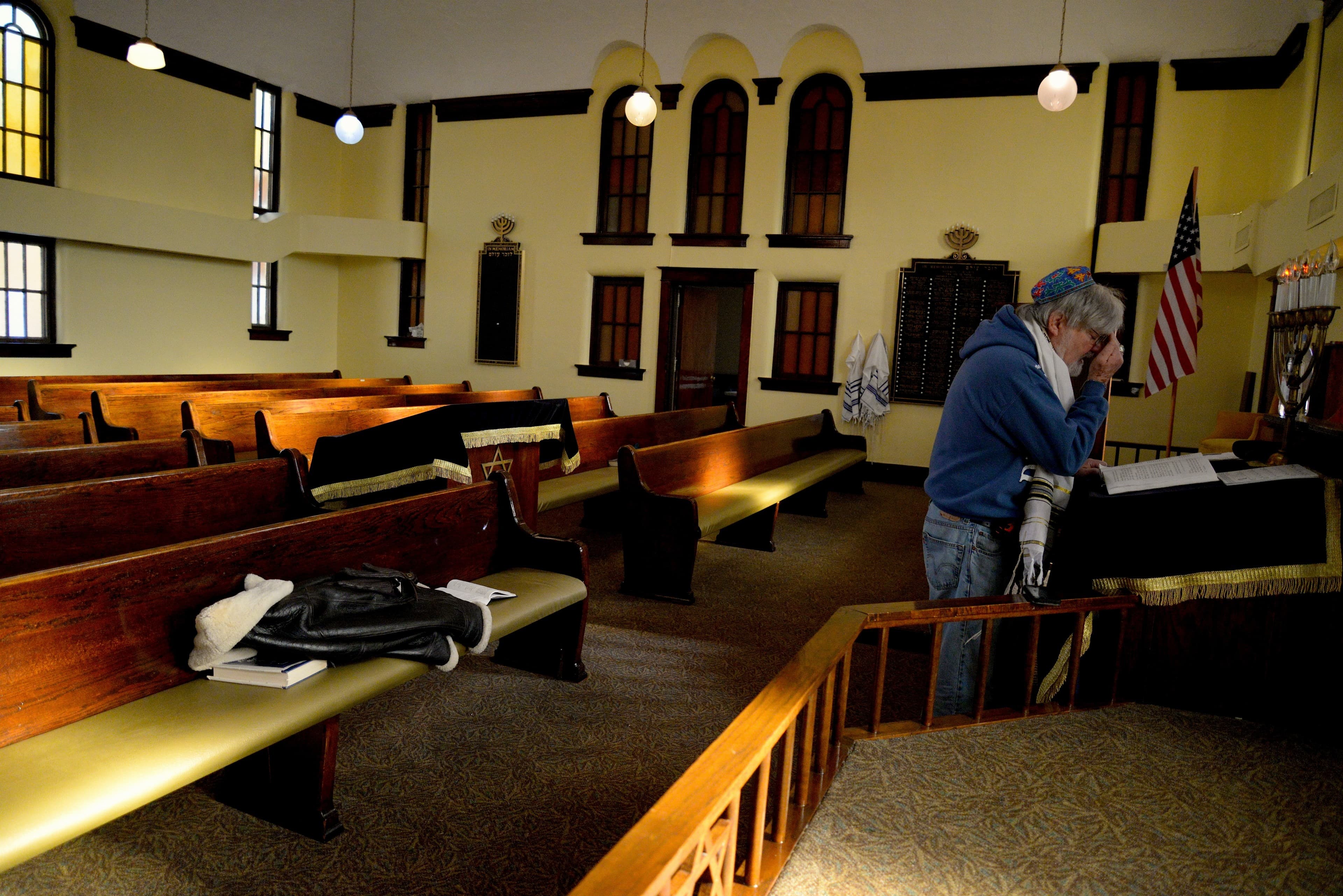 Jewish man prays at altar with pews behind him, USA flag in background