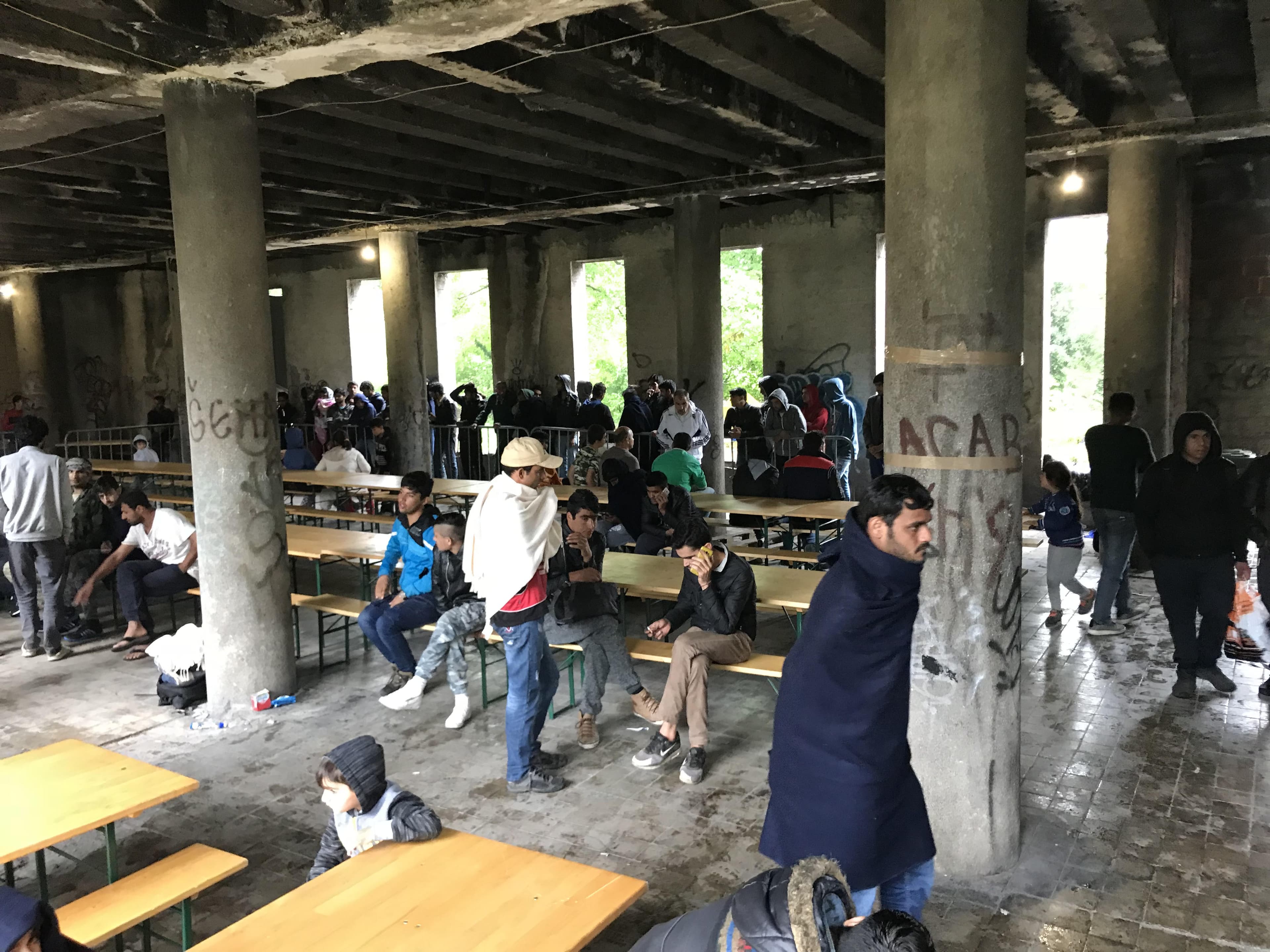 Migrants eat at tables in a makeshift mess hall in an informal migrant camp