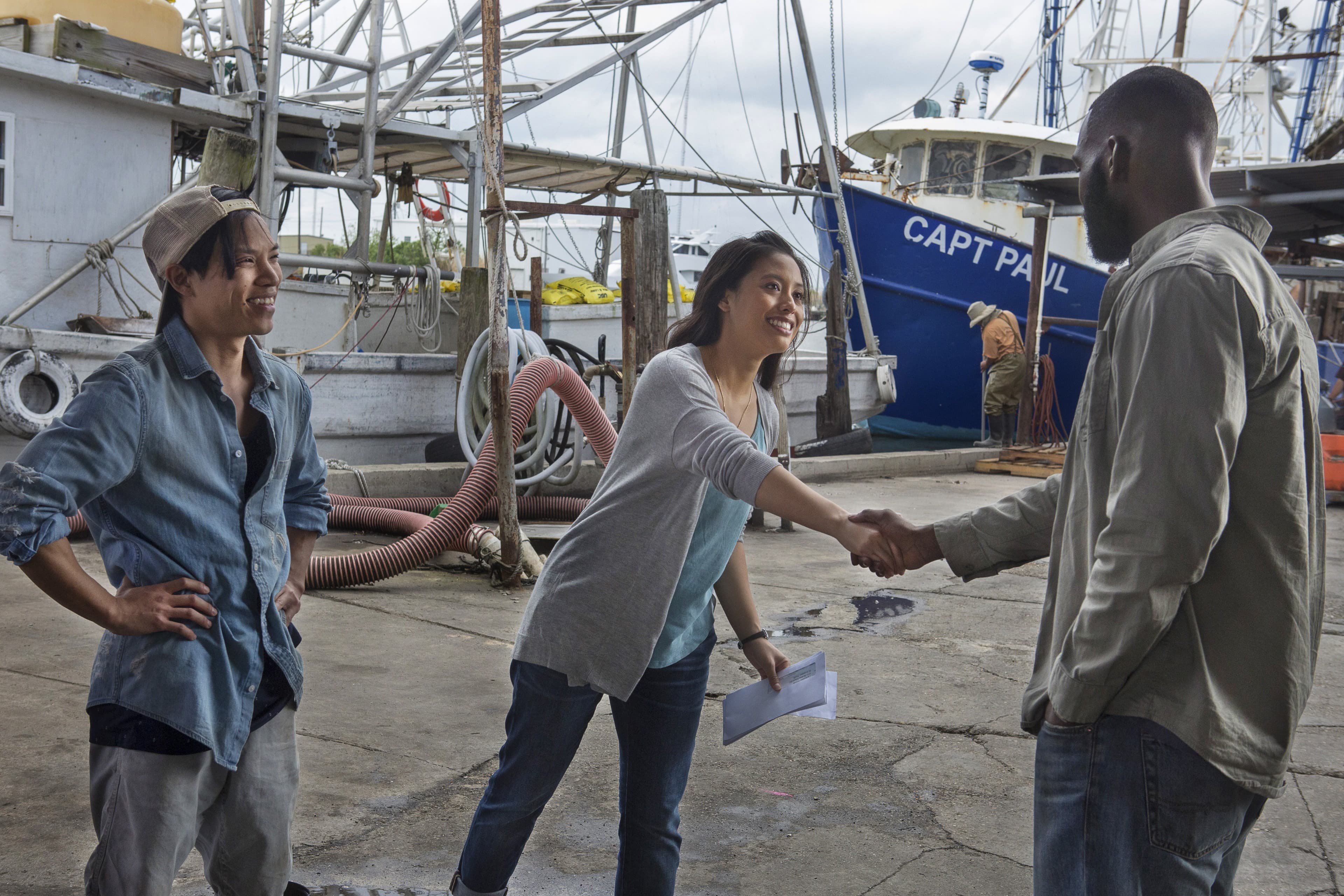 Woman shakes man's hand in front of shipping yard, young man smiling off to the side