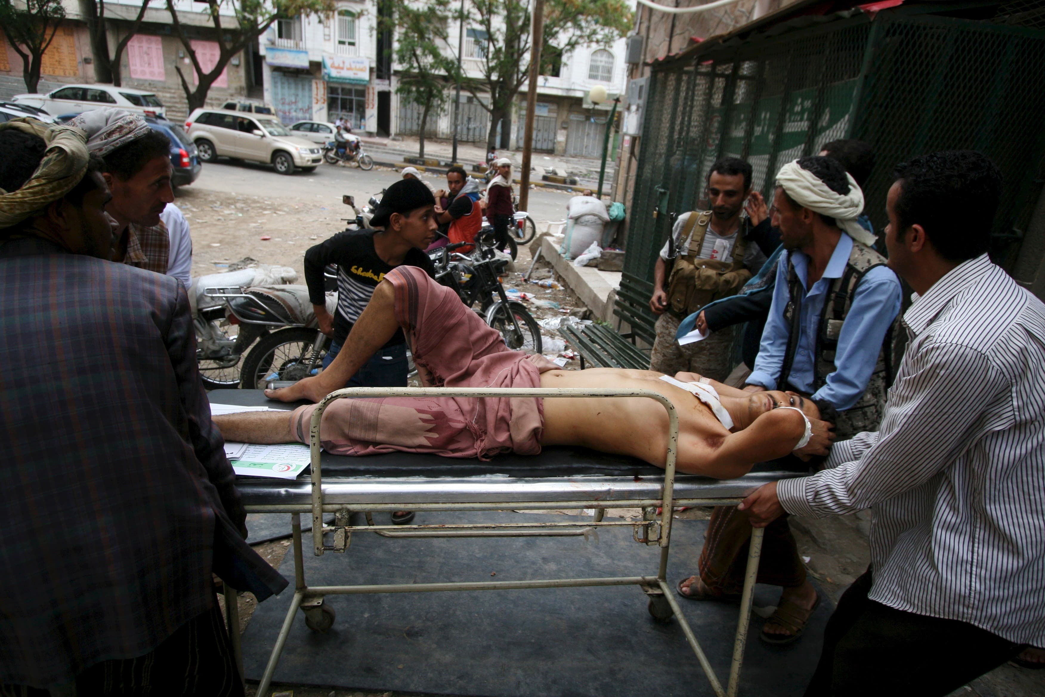 Man on a stretcher, injured, is carried by small group surrounding him