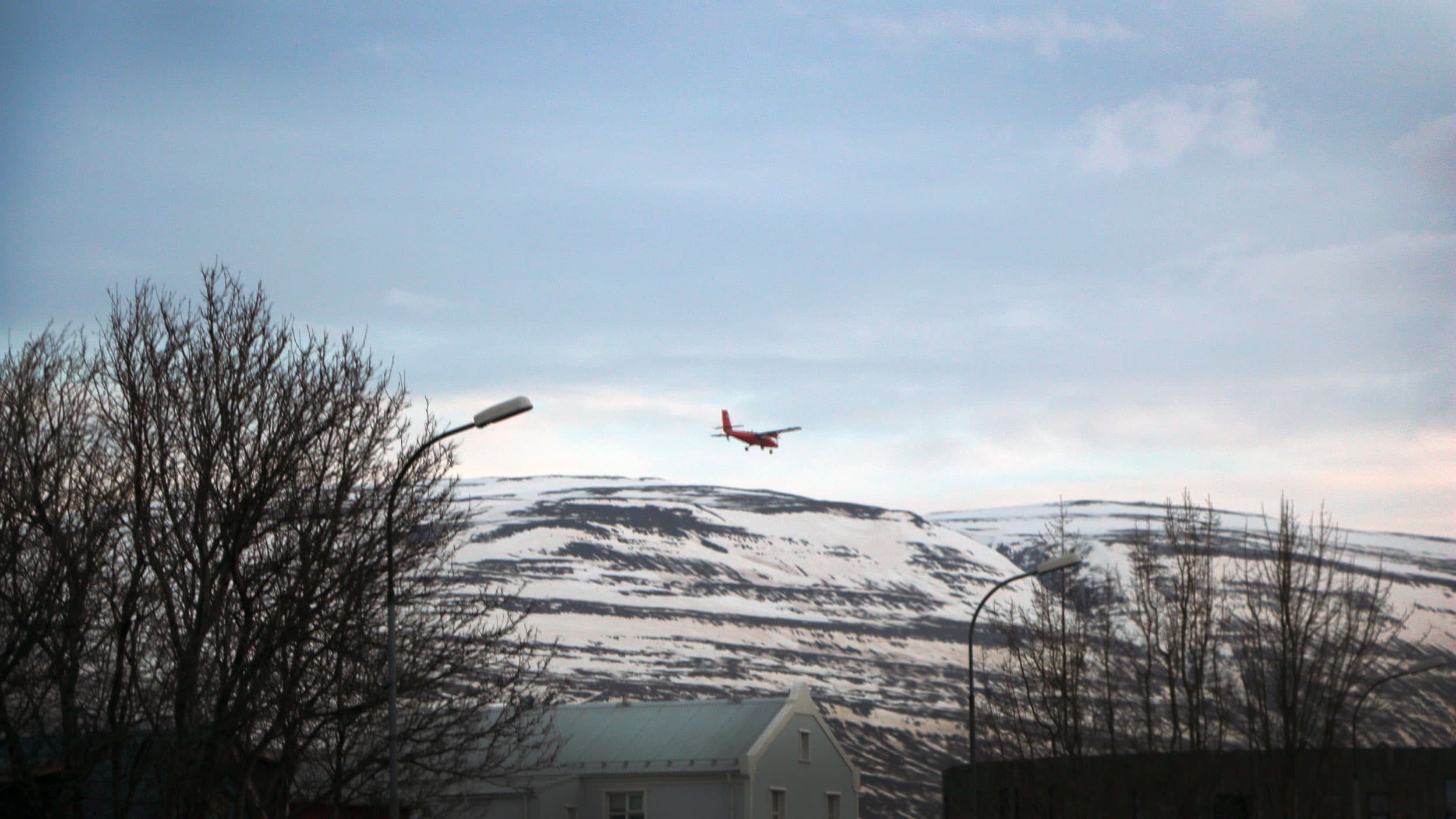 A red plane is seen in the sky above snow covered mountains and a small village