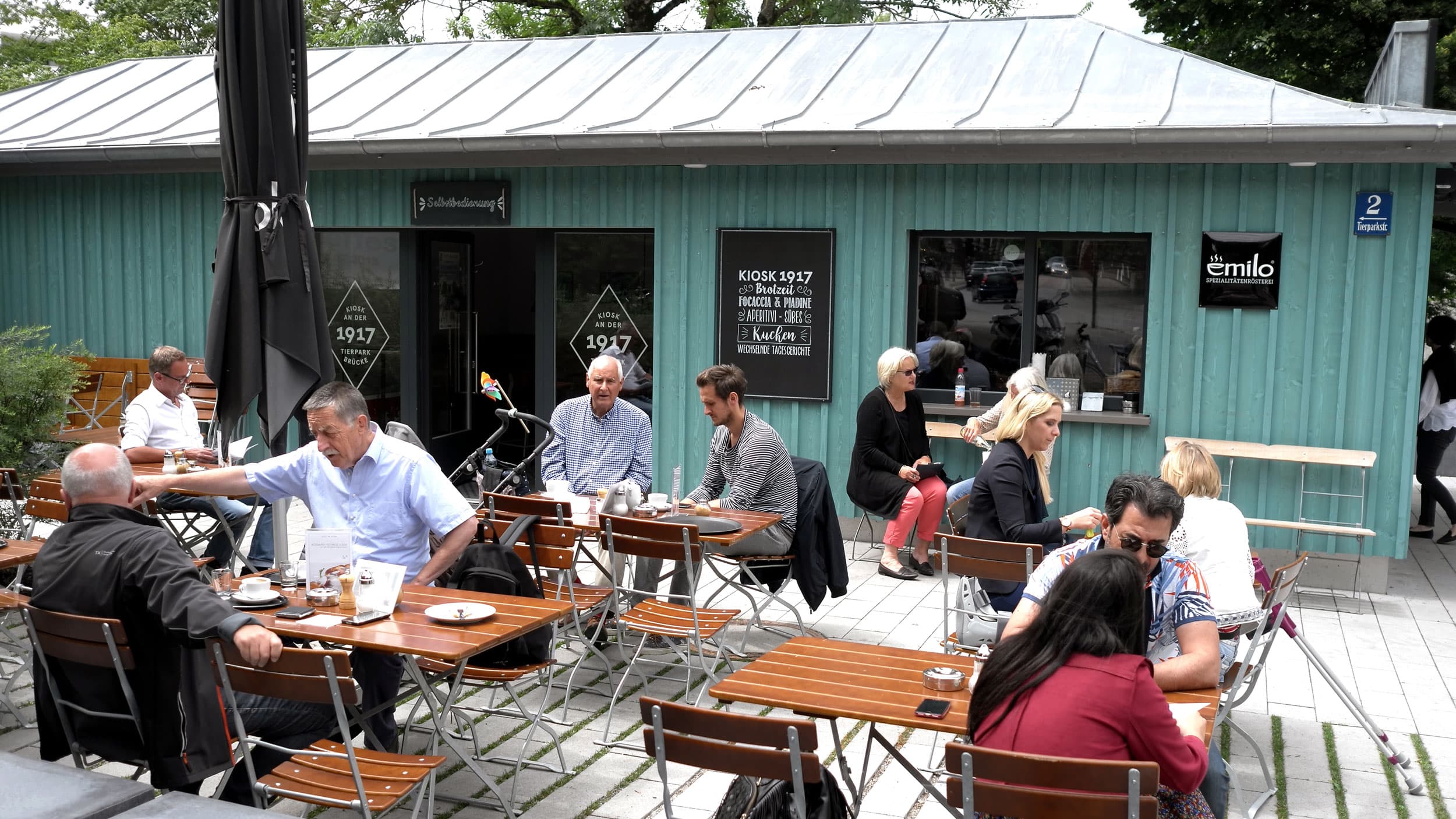 People sit at tables outside a coffeehouse and sip out of white ceramic mugs.