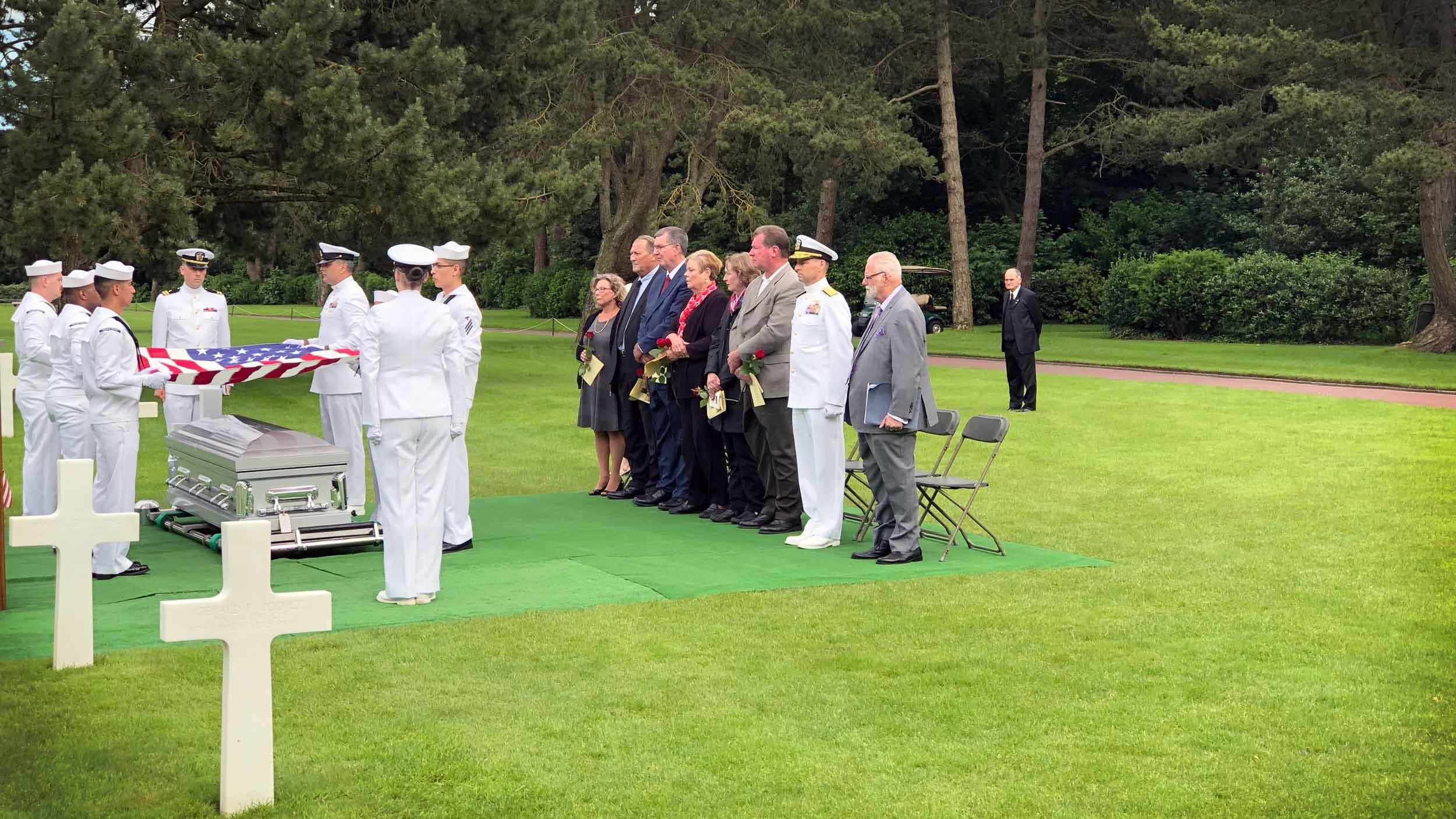A group of people stand opposite another group in military uniforms. There a coffin draped with the American flag.