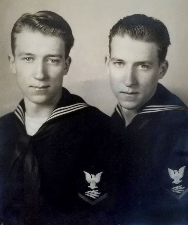 Two young men are pictured in military uniforms from the 1940s. They are twins.