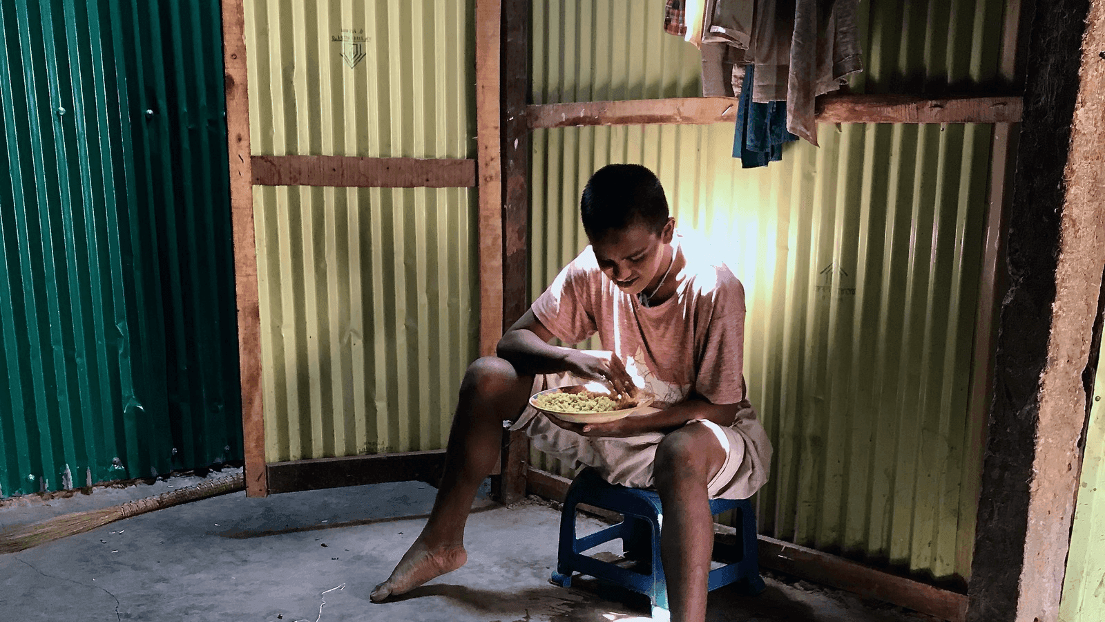 a young Rohingya man with intellectural disabilities sits in his makeshift home