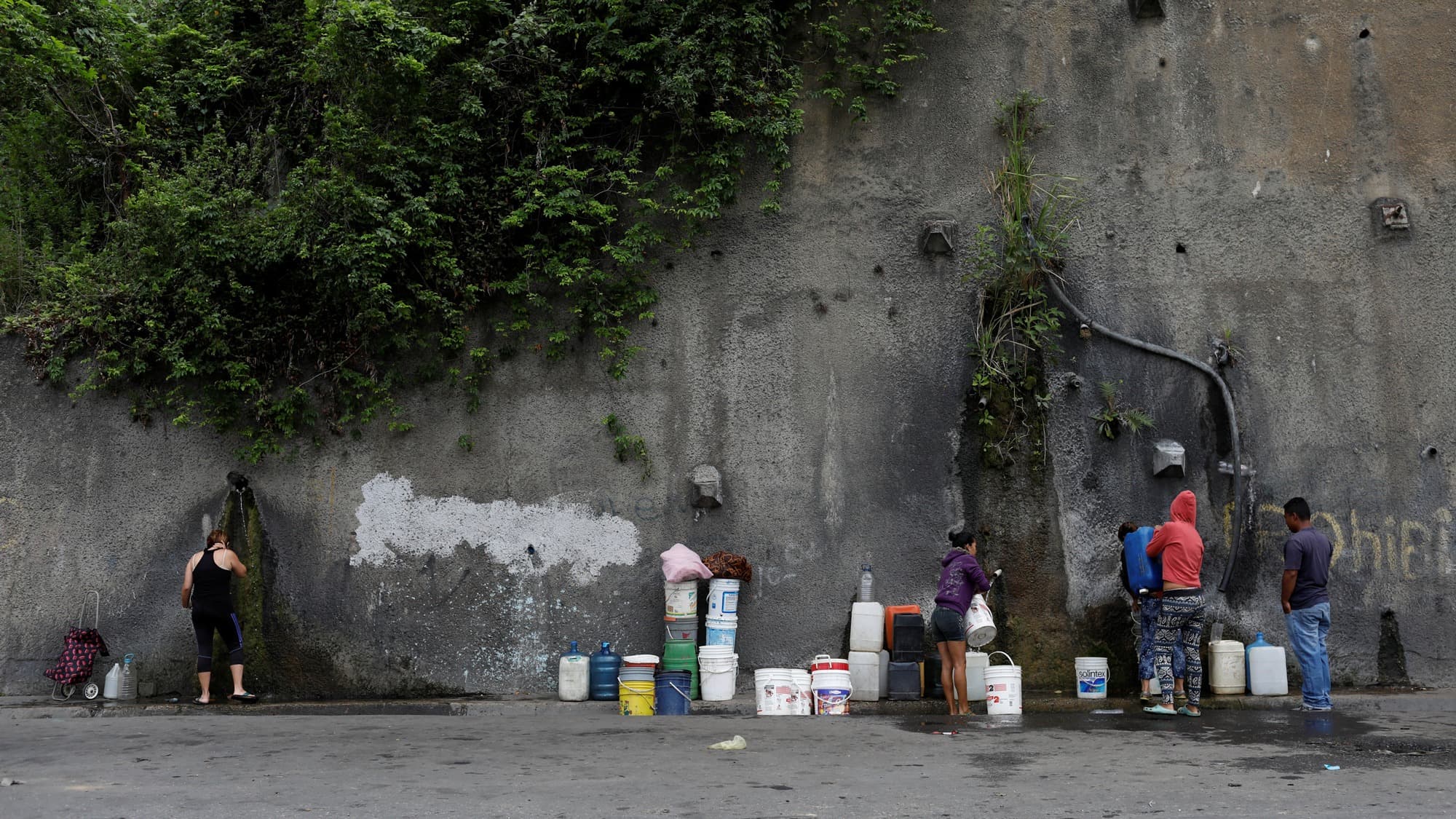 This this wide framed photograph, people fill containers with water coming from a mountain, in a road at Plan de Manzano slum in Caracas, Venezuela.