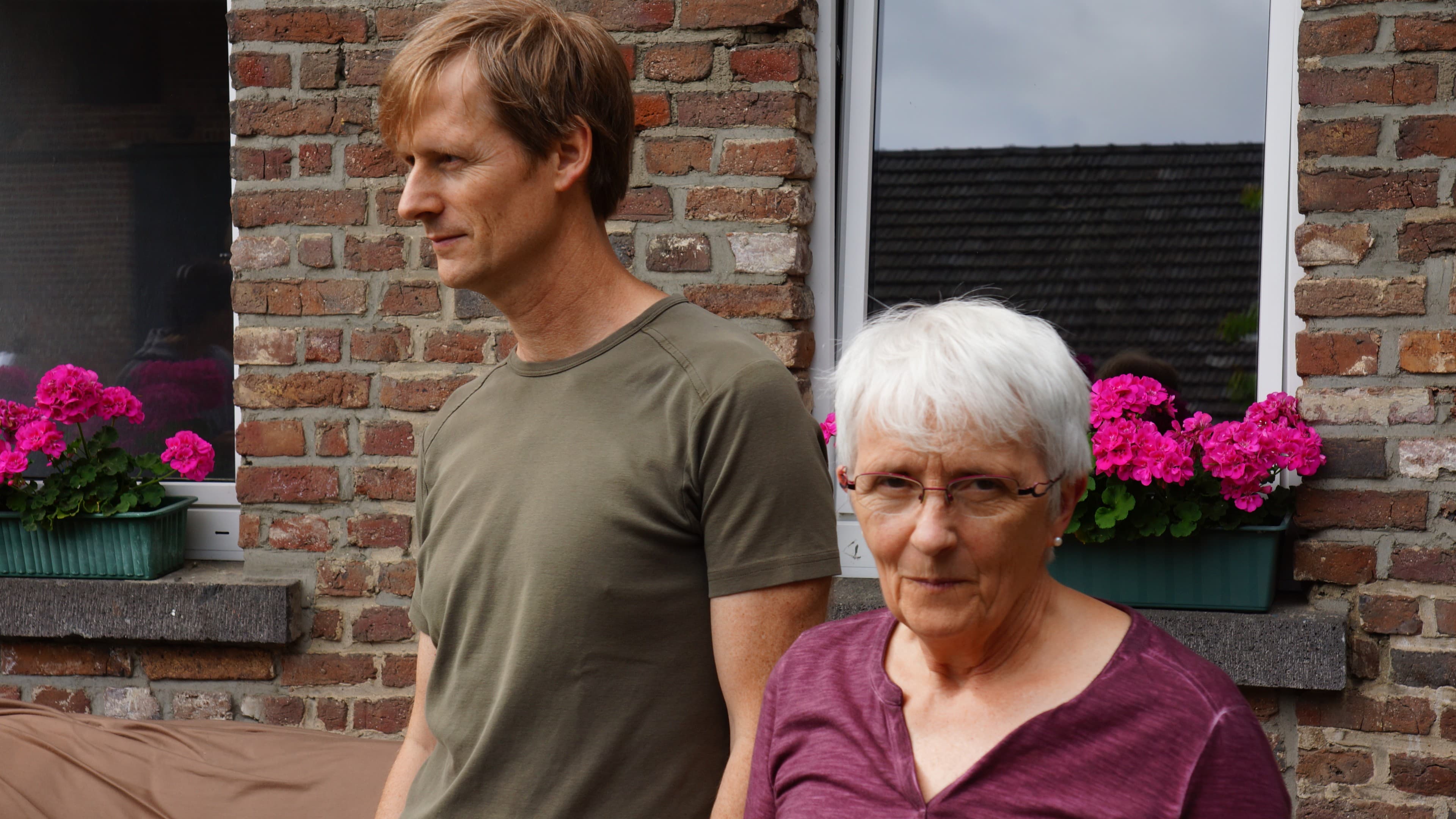 a man stands with his mother in front of their home in germany
