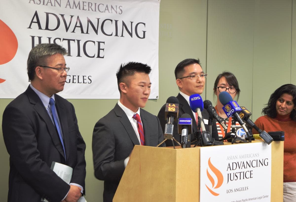 Young man at podium in press conference with signs behind him