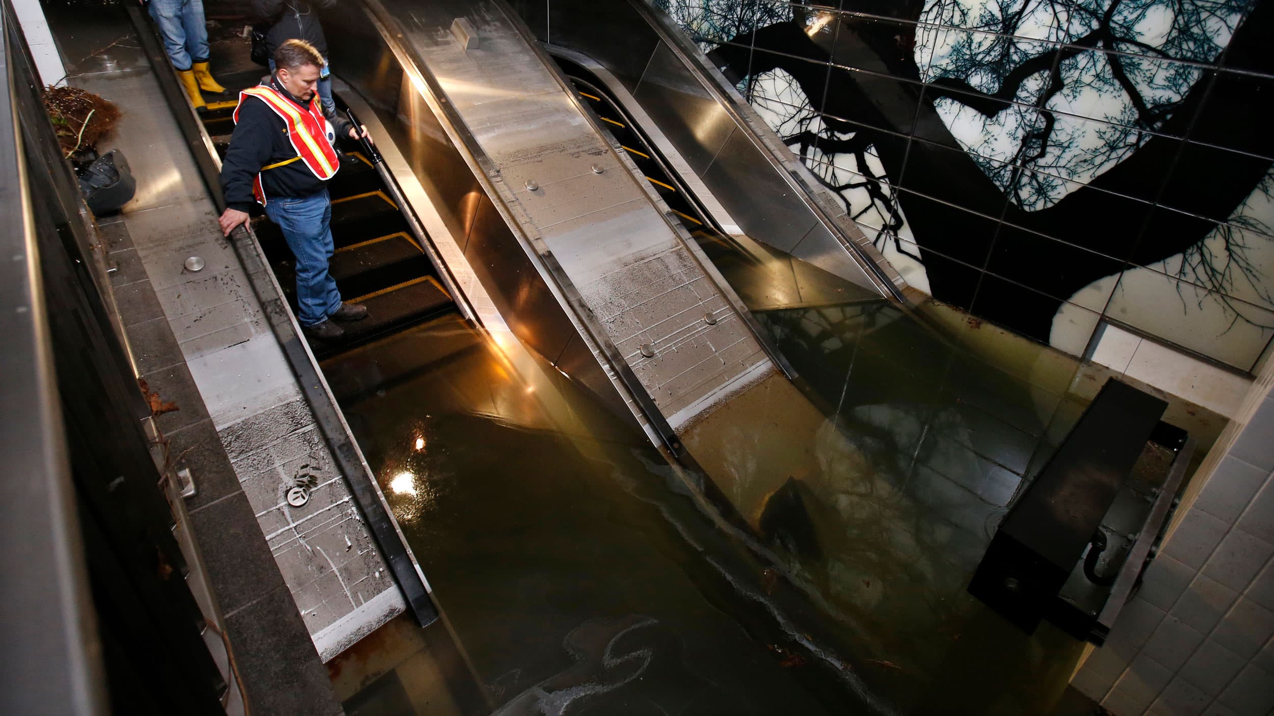 A man stands on an escalator looking down into a flooded subway station
