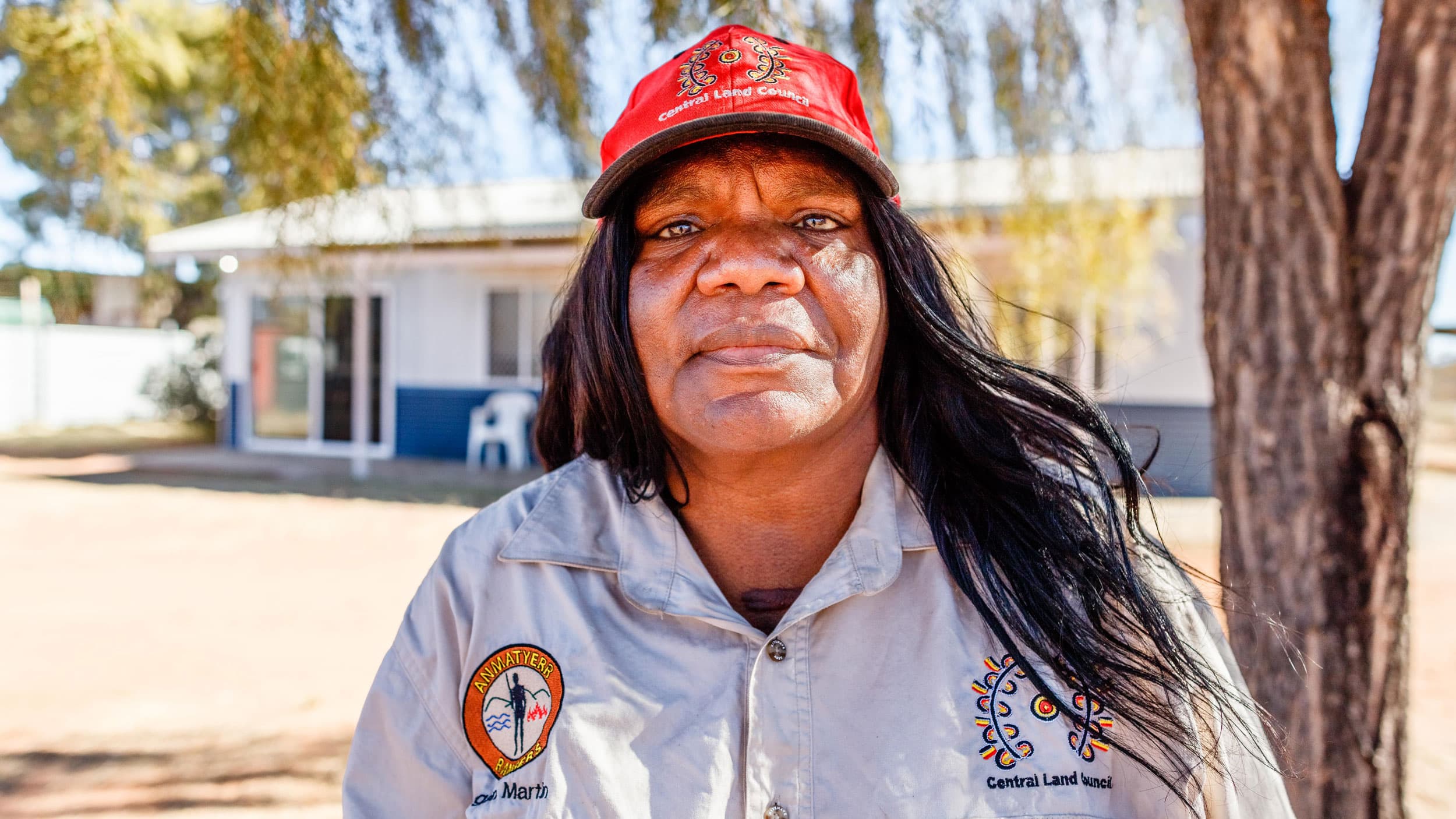 A woman stands for a portrait. She wears a ballcap and a khaki shirt.