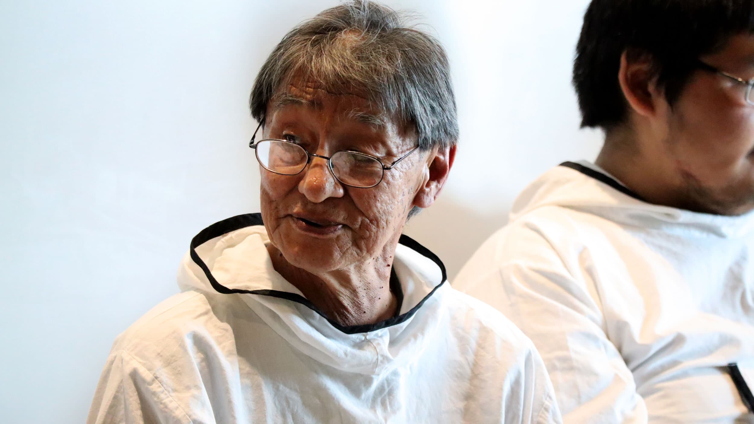 An older man wears glasses and a white shirt