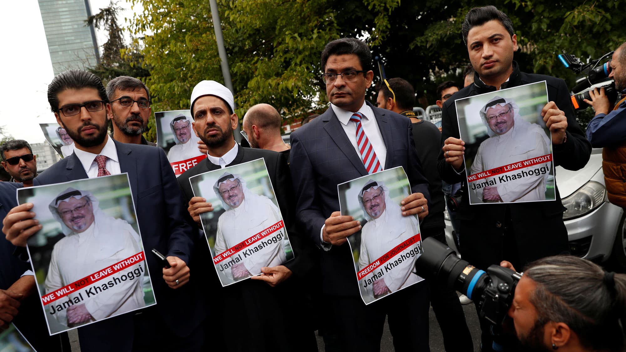 Four men wearing suits stand abreast holding posters of Saudi journalist Jamal Khashoggi's picture.