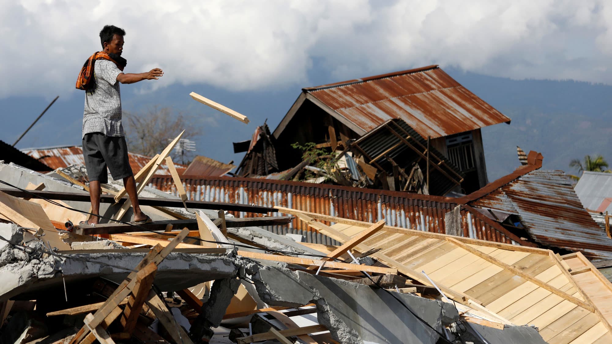 A man is shown throwing a piece of wood from the ruins of a house in in Palu, Indonesia.
