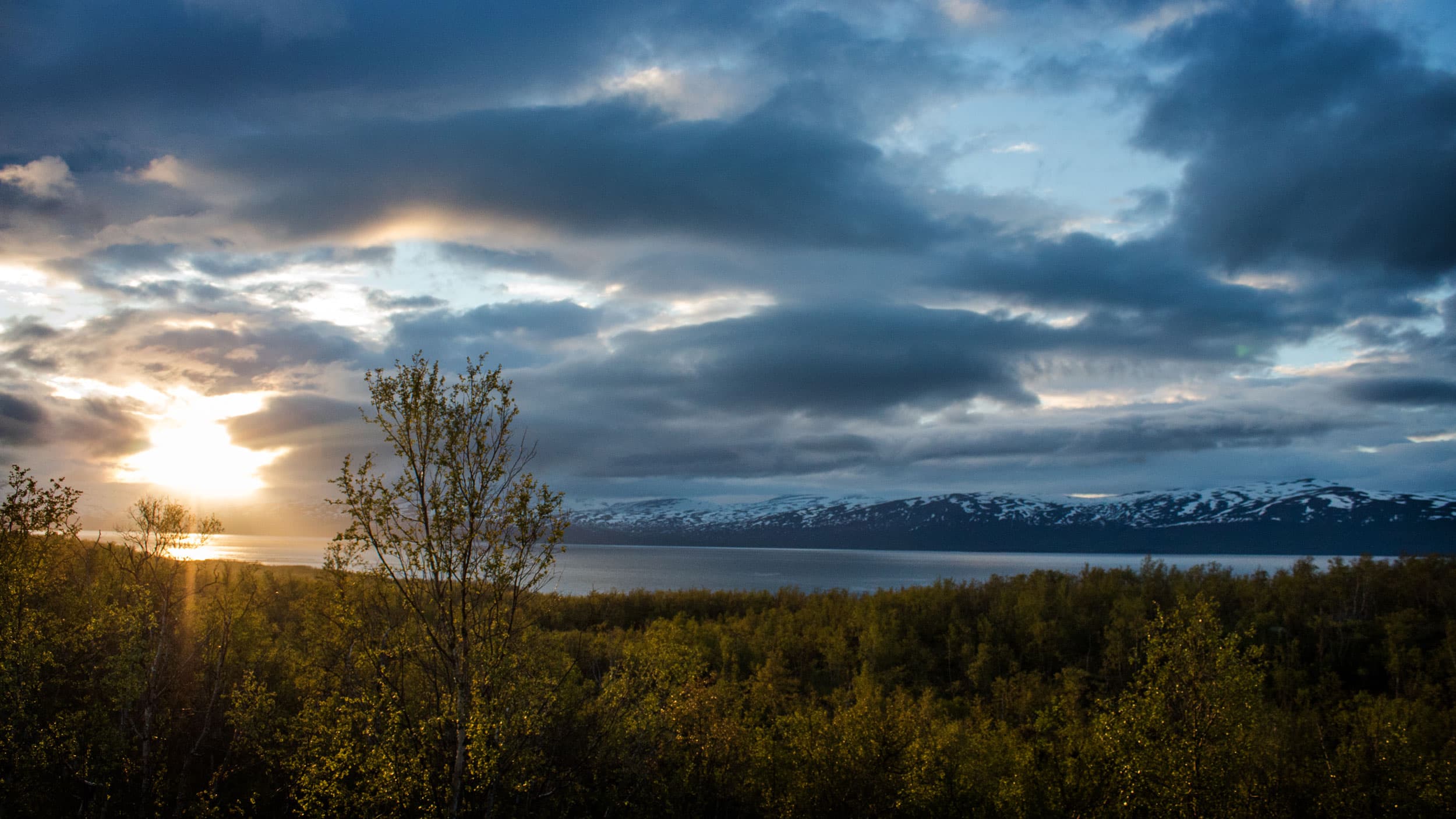 A sun sets behind a cloud over a grey body of water