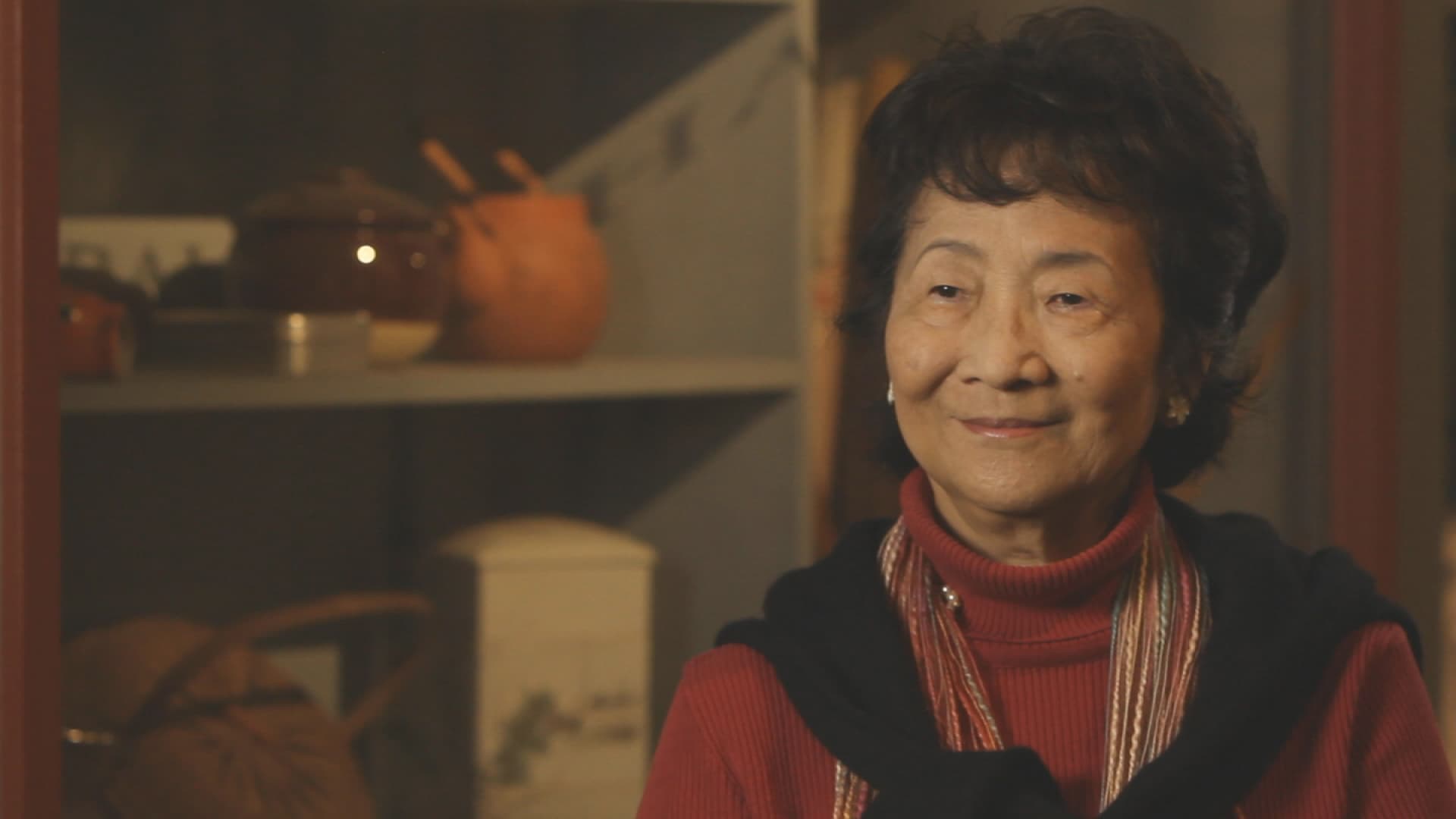 A seated older woman in a red top looks past the photographer.