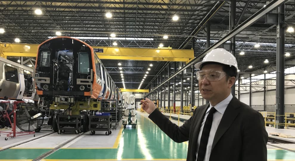 a man with goggles and a protective helmet points to the factory behind him