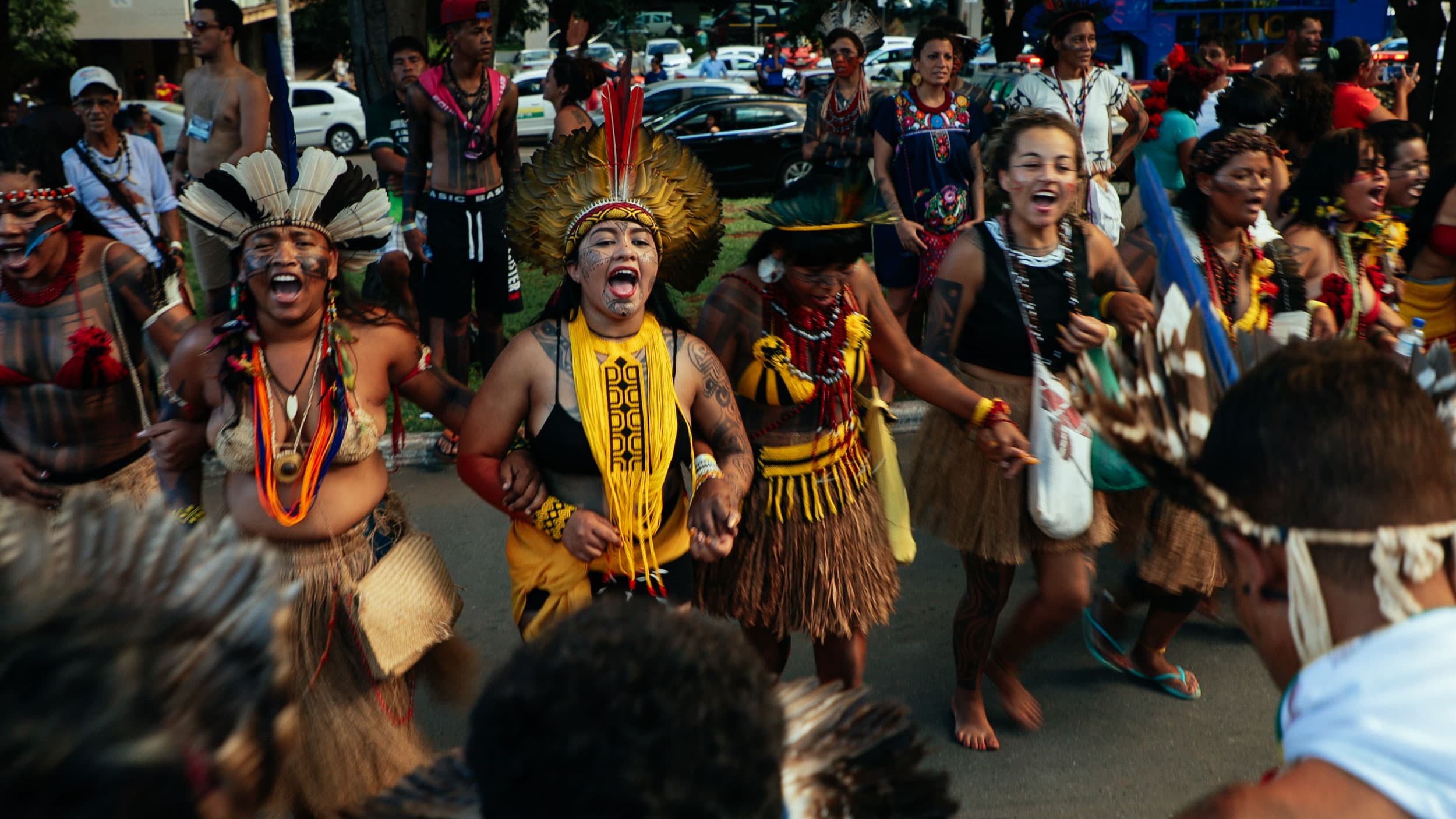 Women in headdresses and beads link arms in a line during a protest