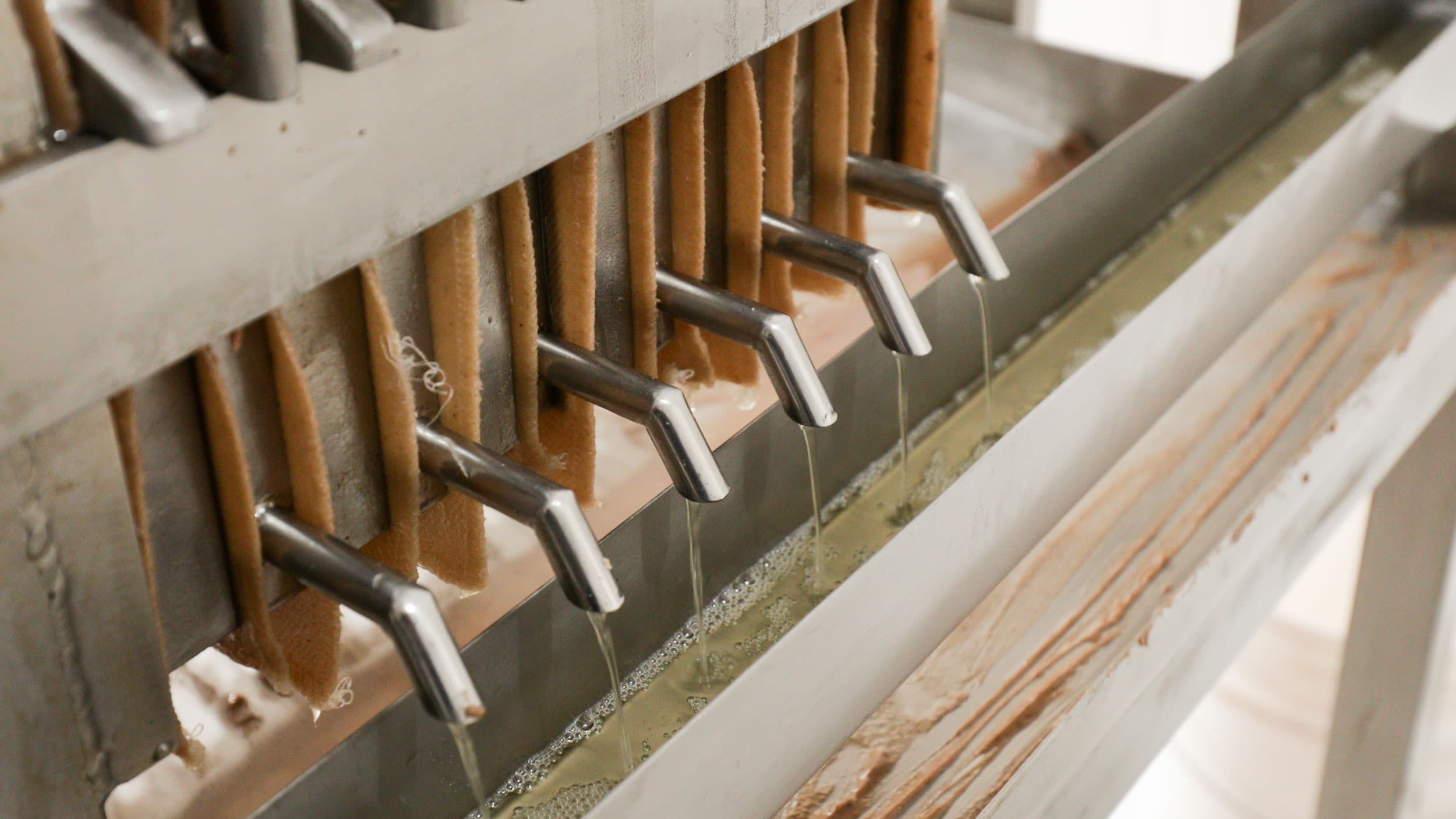Thin strand of oil run out of metal pipes into a trough below