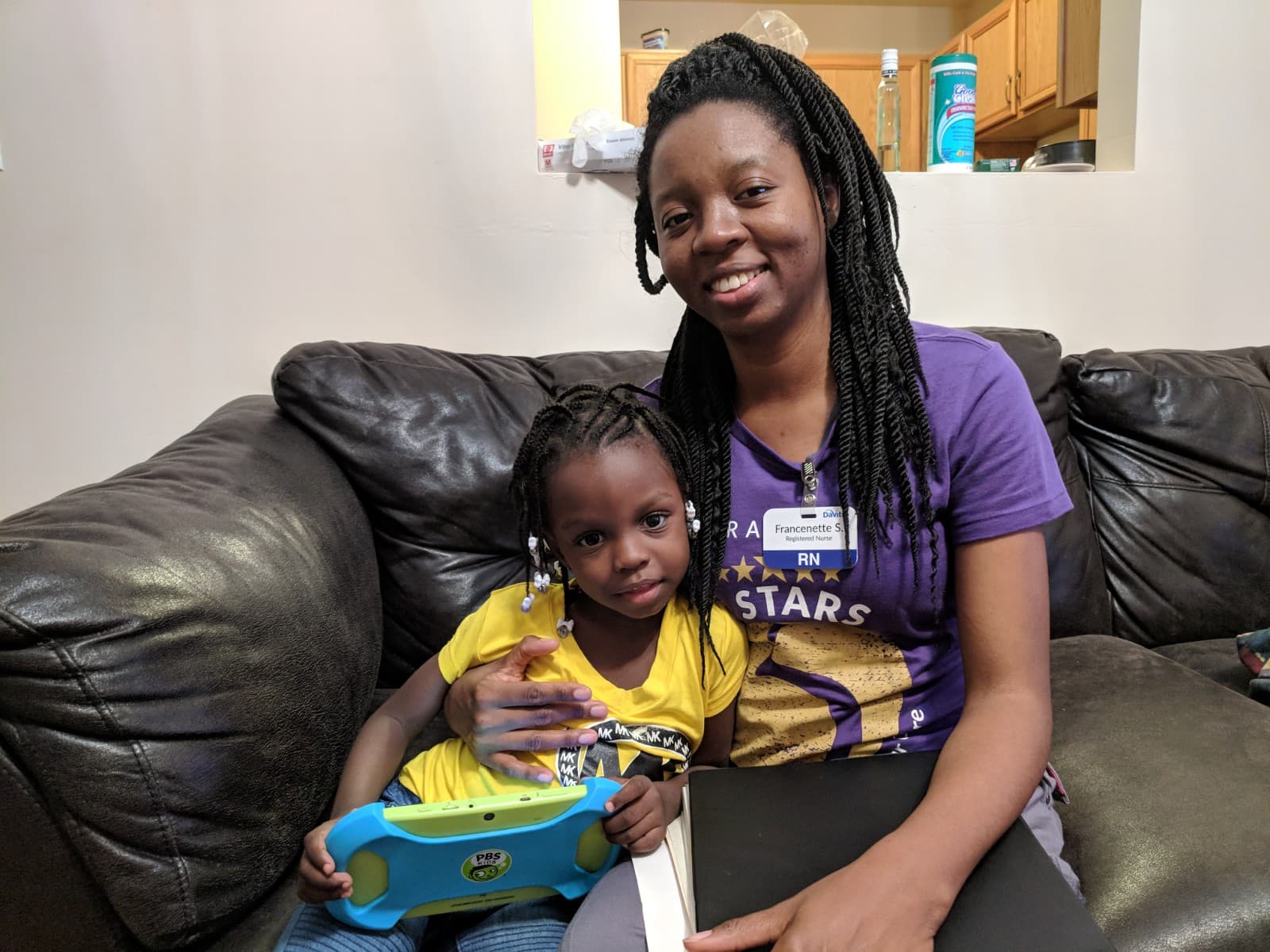 Woman sitting on sofa with young girl leaning into her lap, both smiling at camera