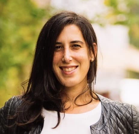 Woman smiling, looking at camera, greenery behind her out of focus