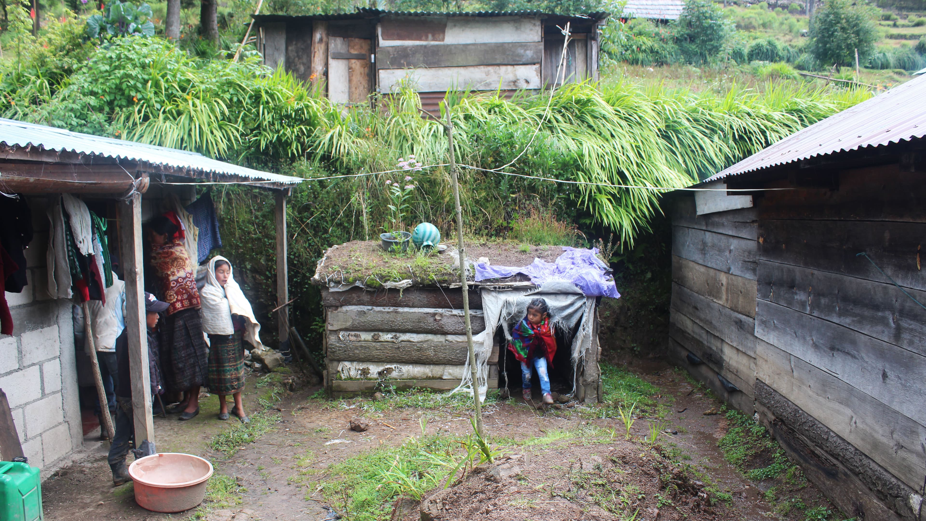 Children play in a dirt yard between two huts.