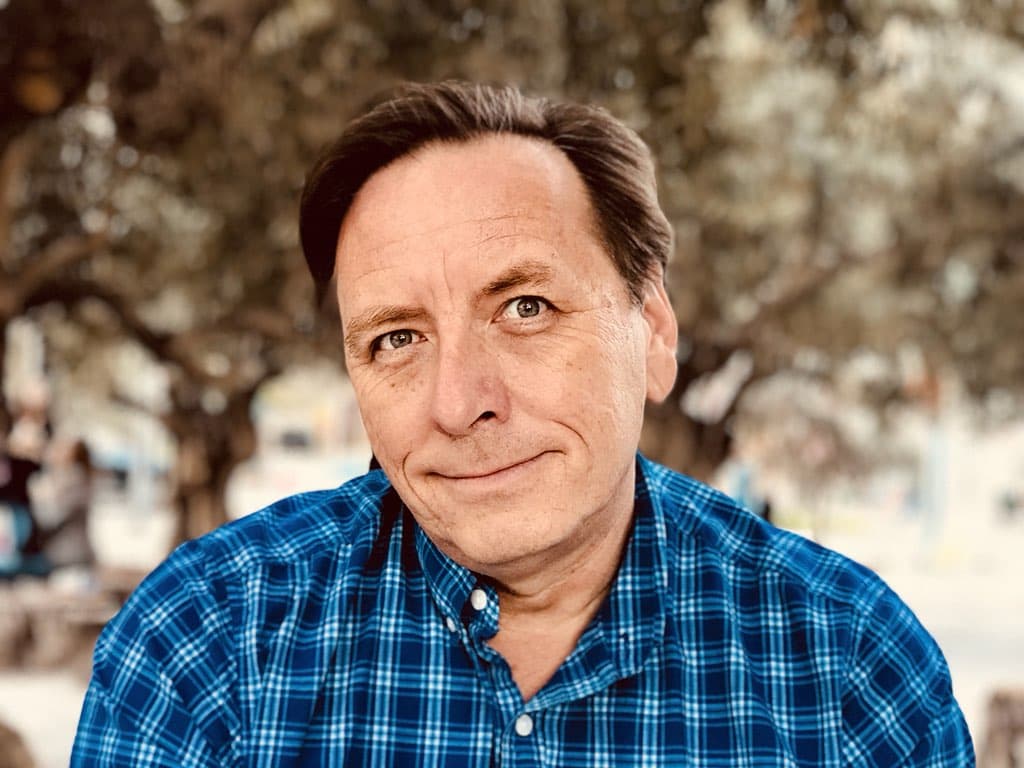 Portrait of man in plaid shirt with trees in background. He's looking up.