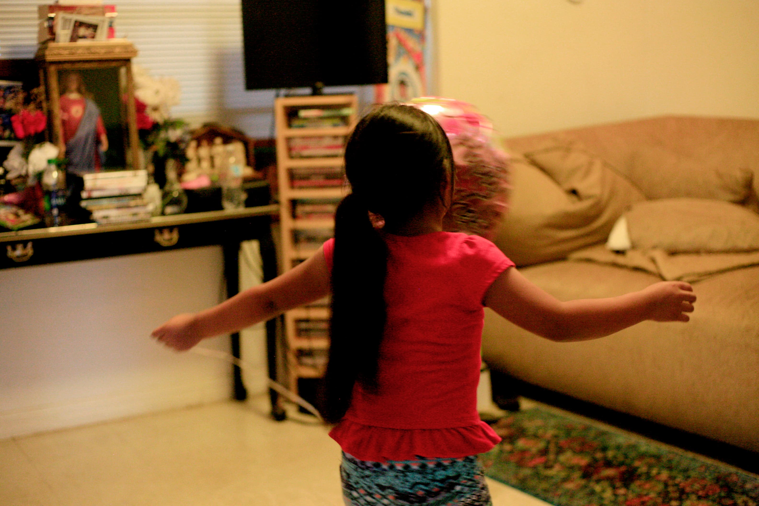 Young girl, shown from behind, with arms outstreched, in room in home