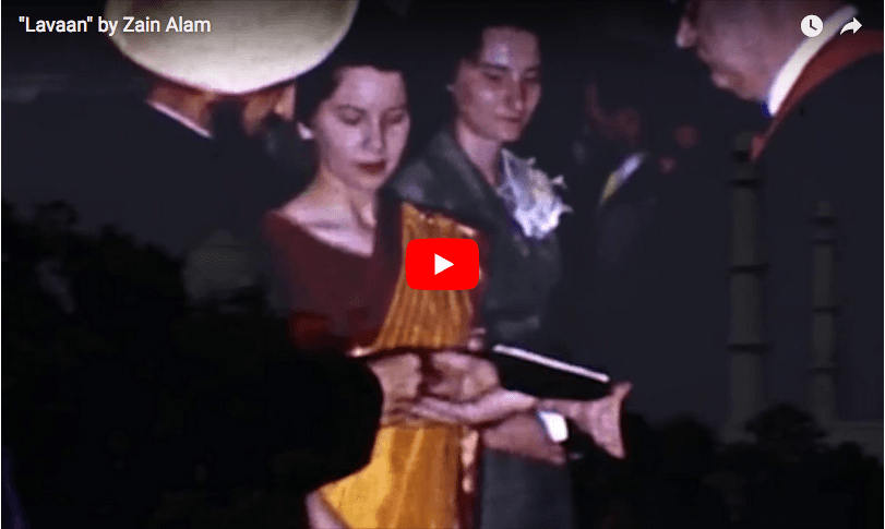 Large screen show grainy footage of woman in sari, man in turban. A silhouette of a man standing in front.