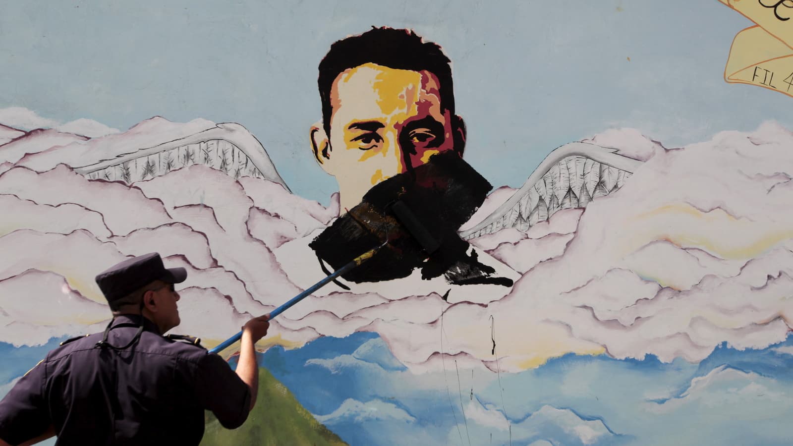 A man paints over graffiti of a face associated with a gang.