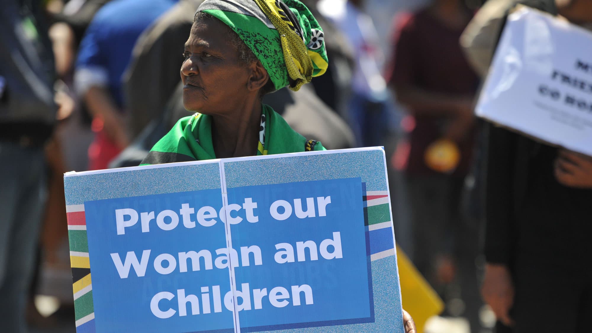 A woman protestor holds a sign that says protect our women and girls