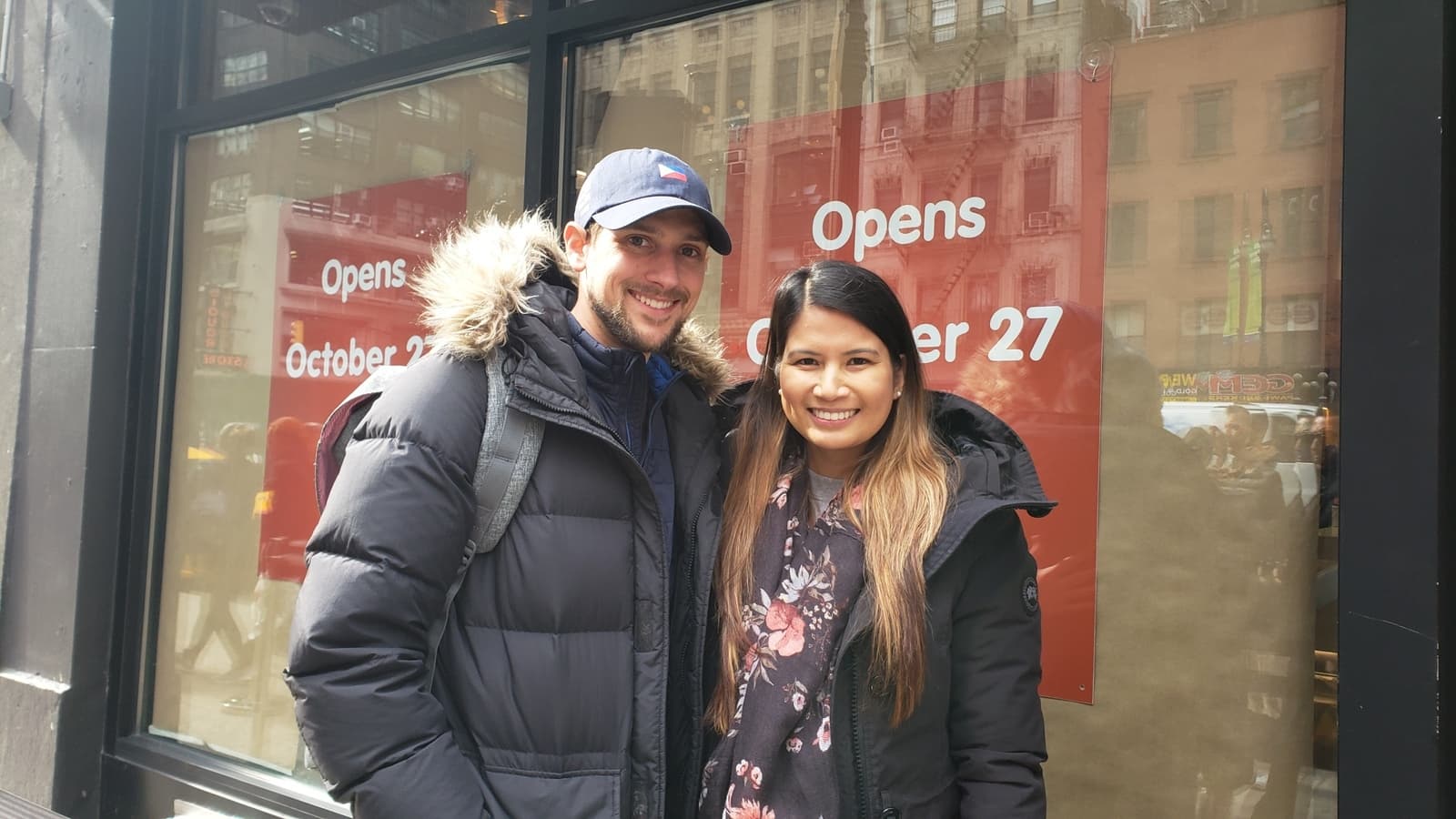 A man and woman wear winter gear while waiting in line at Jollibee.