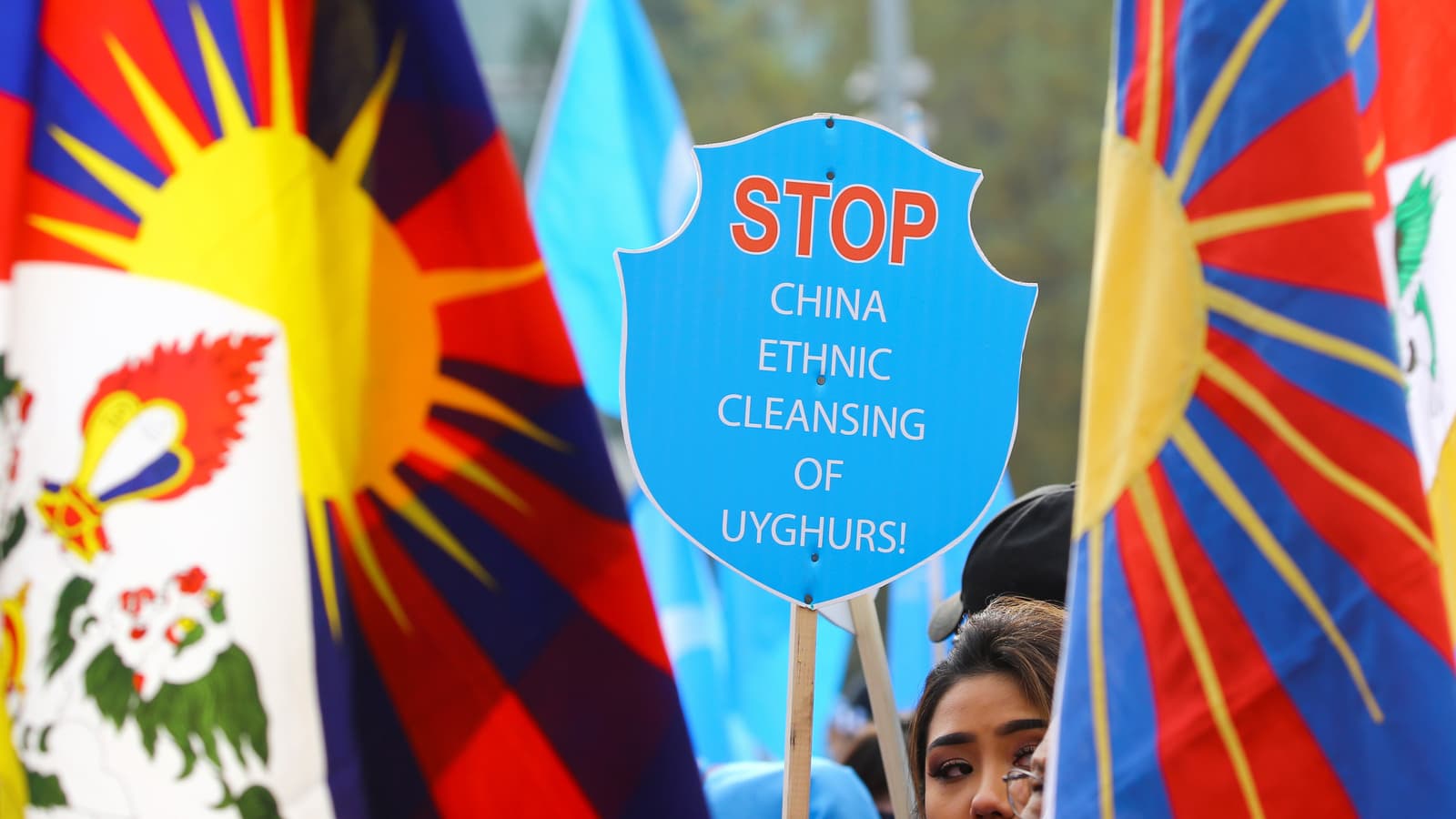 A woman's face appears amidst colorful signs protest against China's Uyghar detention centers.