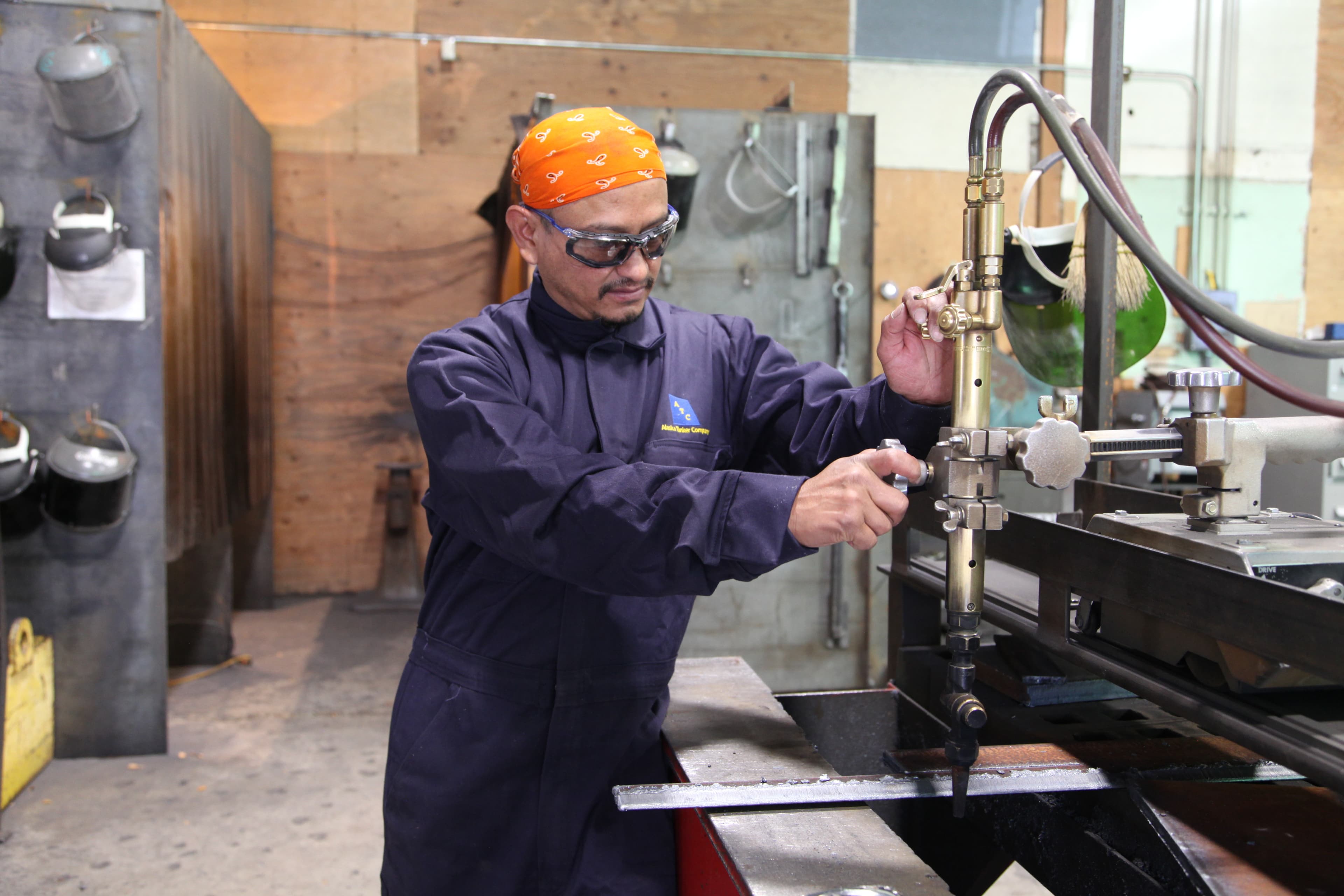A man in welder's coveralls uses machinery in a workshop