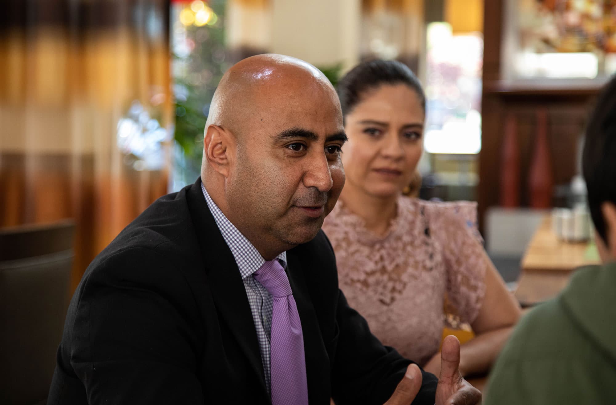 Art Gallegos is shown wearing a suit and tie sits at a table.