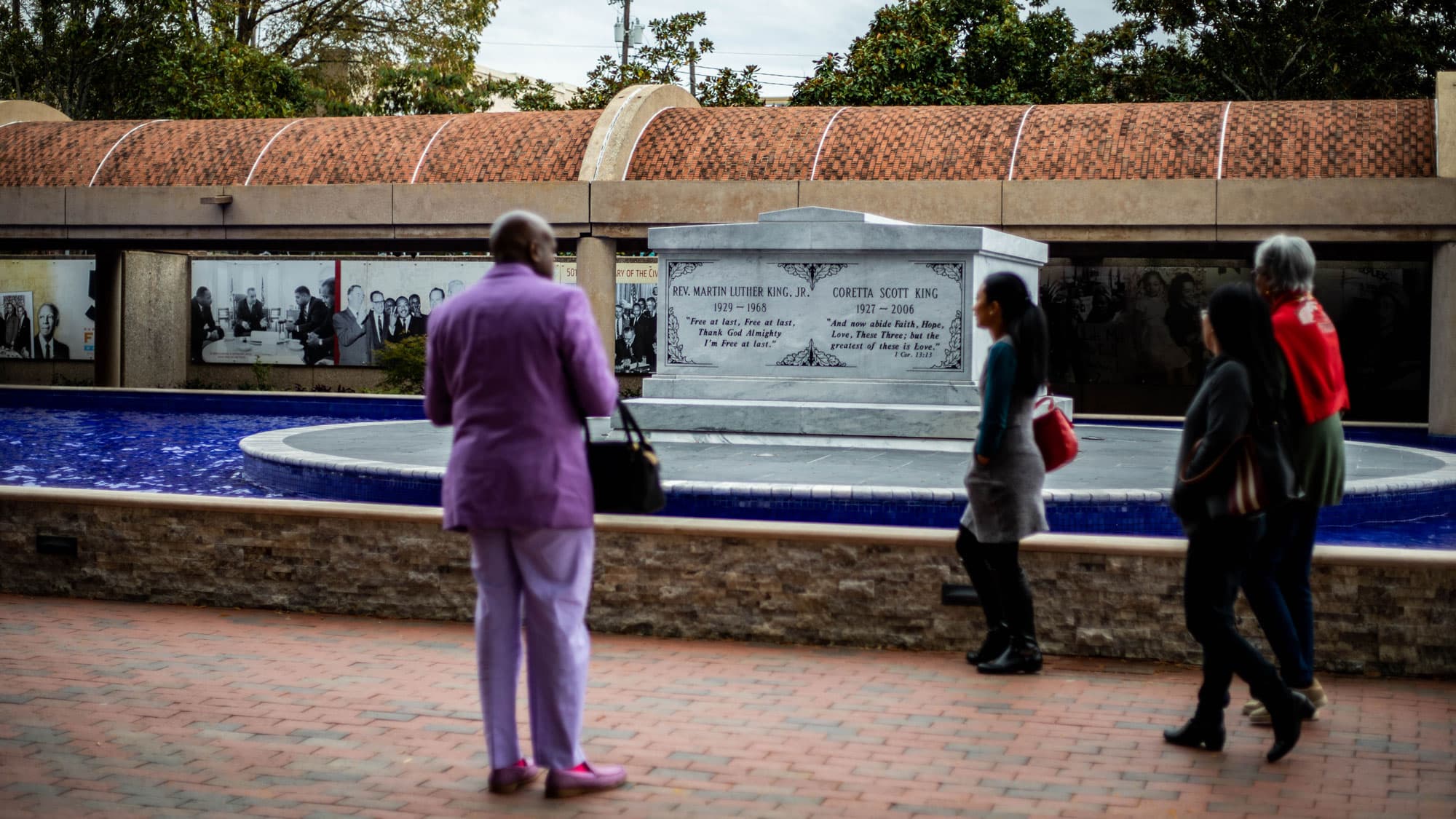 Several people including a man wearing a purple suit, look on at the stone monument for Martin Luther King, Jr.