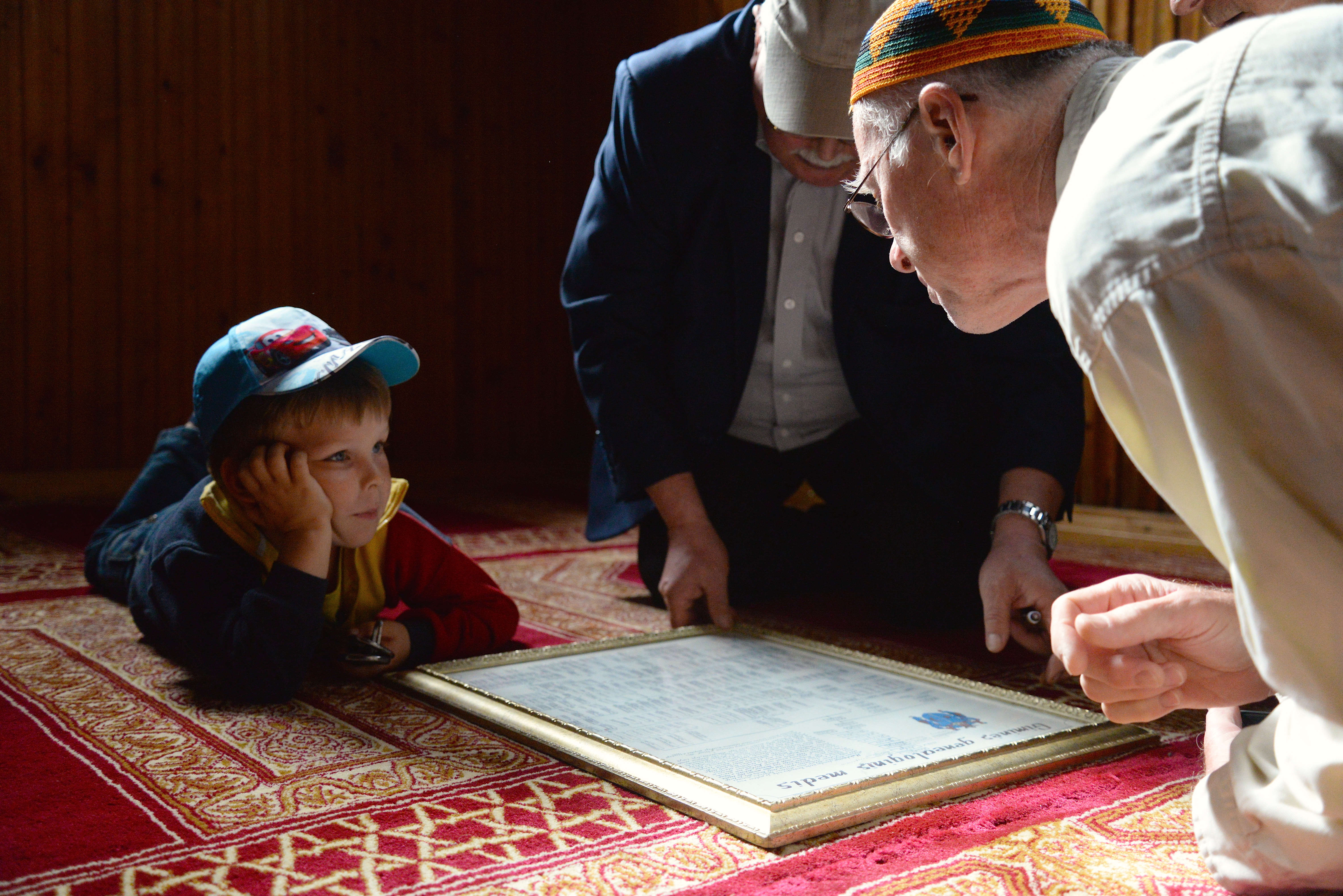 Man leans over scripture with young boy, laying on carpet looking on