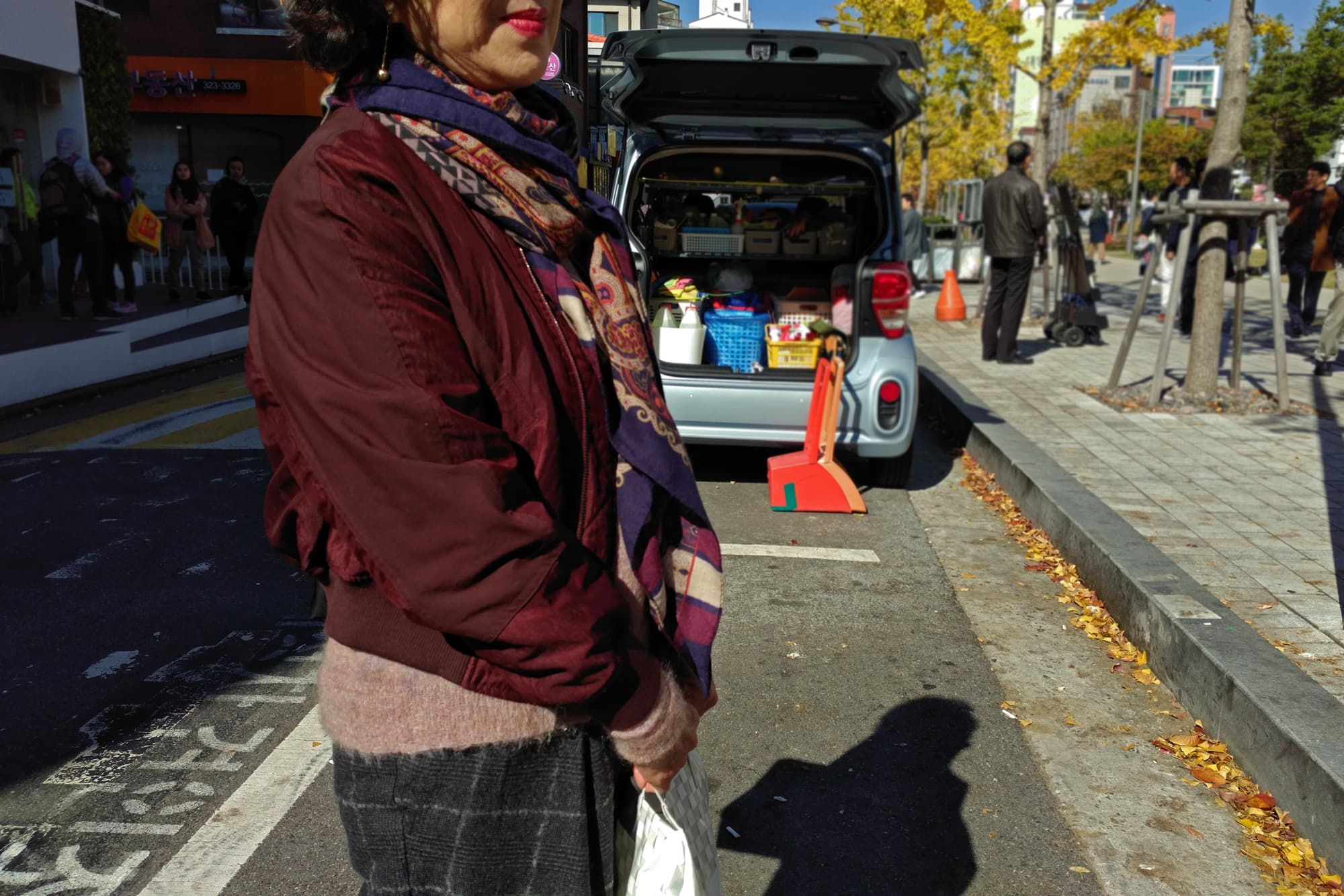 Hong Jung-hee, 68, wears a maroon coat and stands in the street.