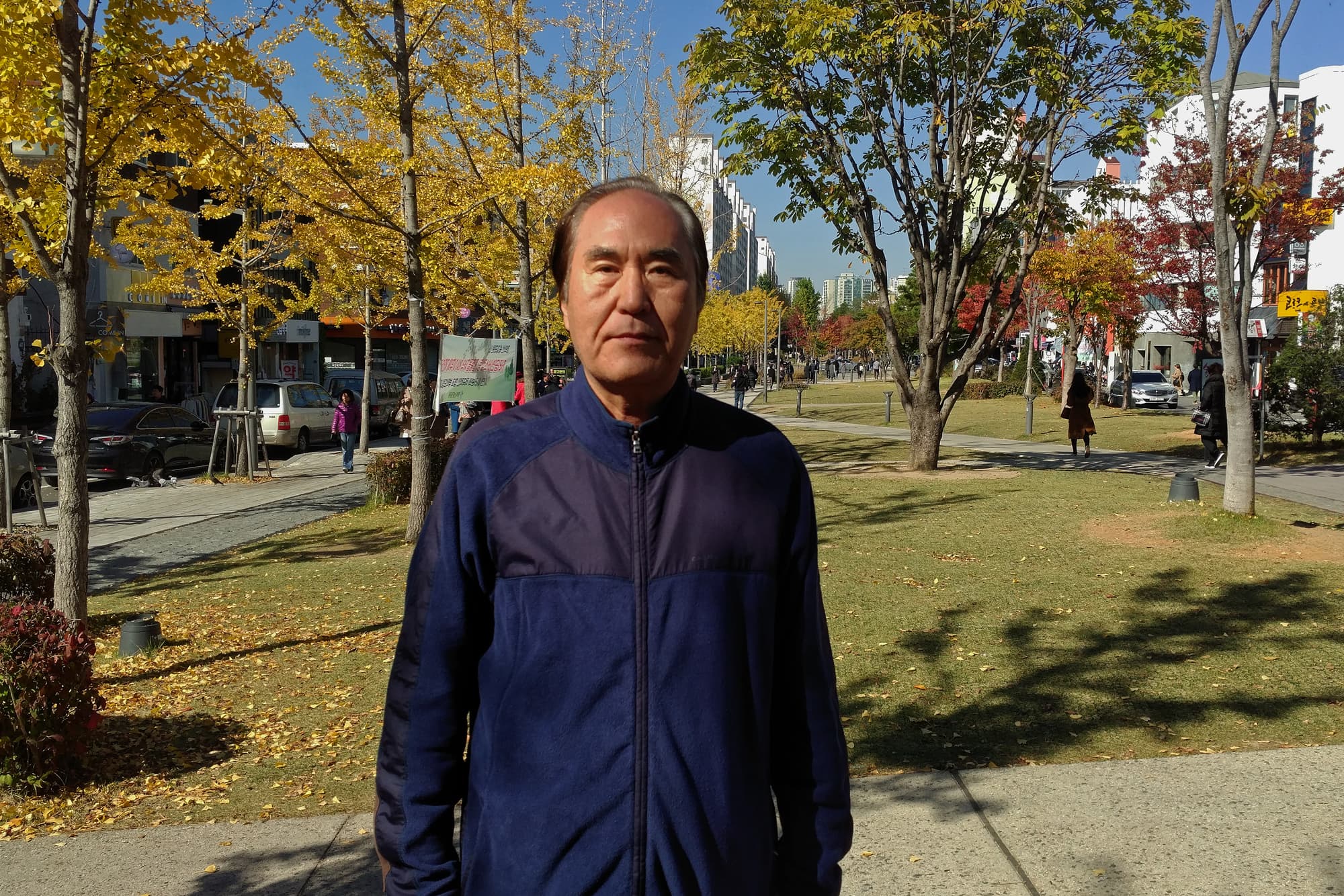 Kim So-il wears a blue vest and stands outside.