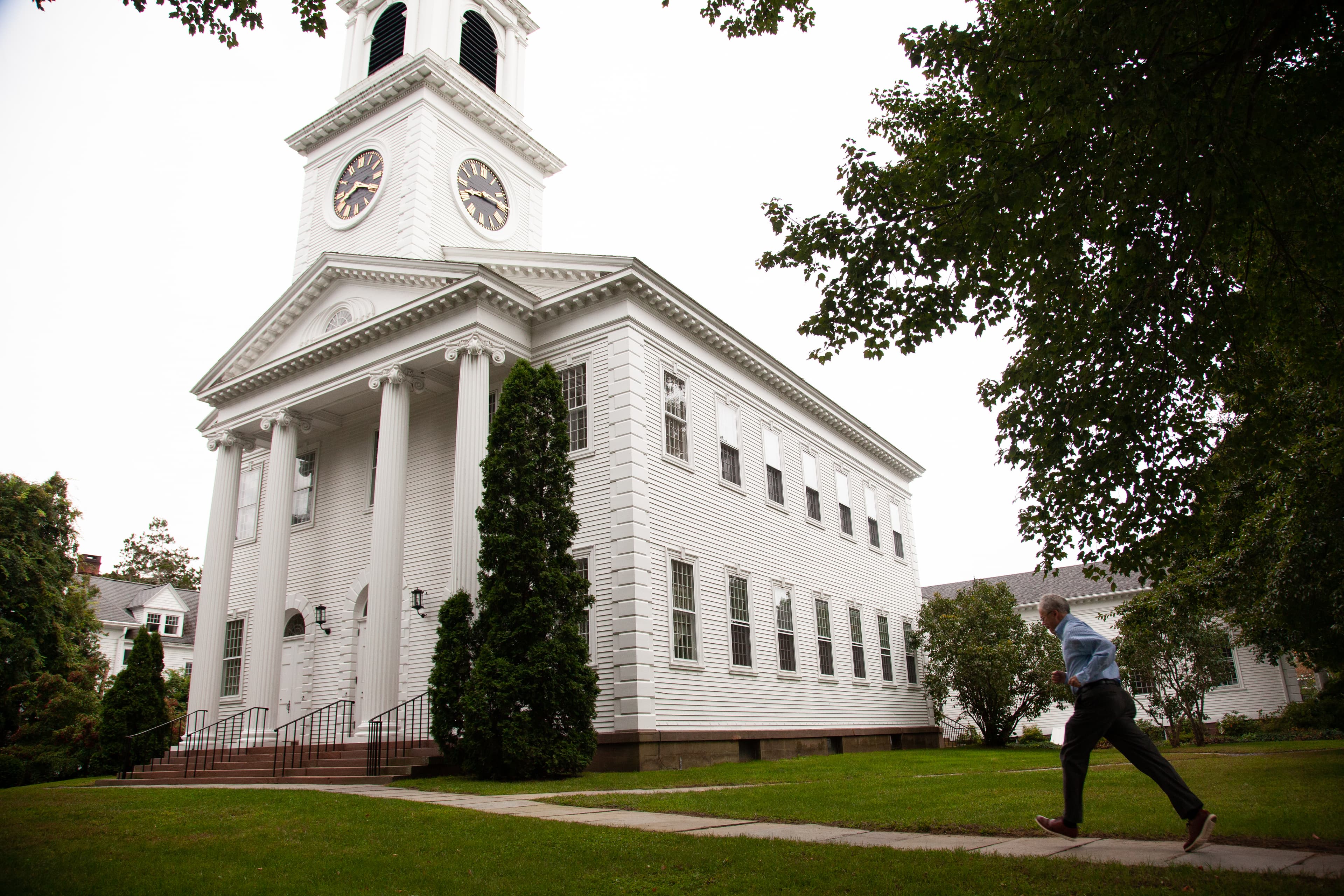 wide shot of two-storey white church, with pillars in front and steeple, man walking on pathway to entrance