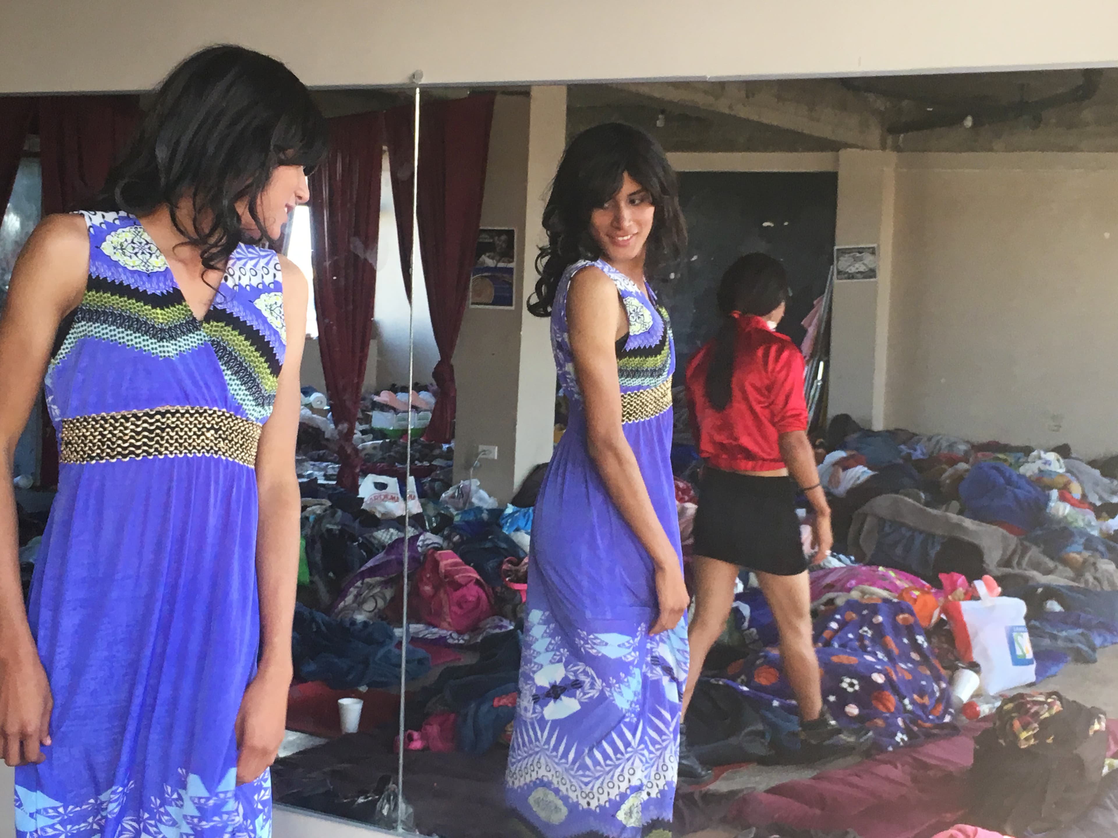 a migrant tries on a purple dress and looks in the mirror