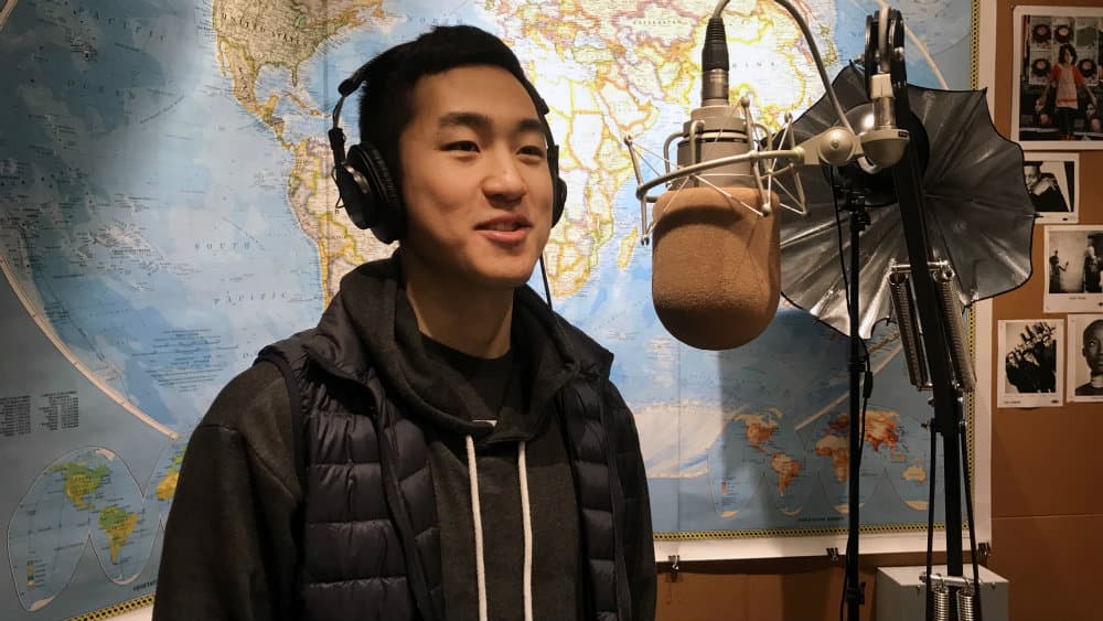 A young man is standing in front of a studio microphone